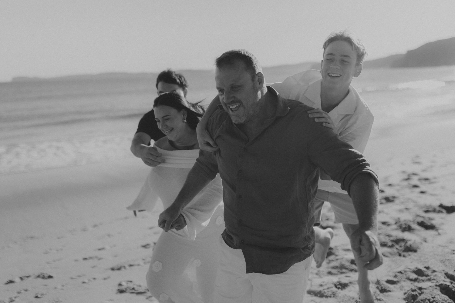 Playful moment captured in black and white as group runs and laughs together on beach.