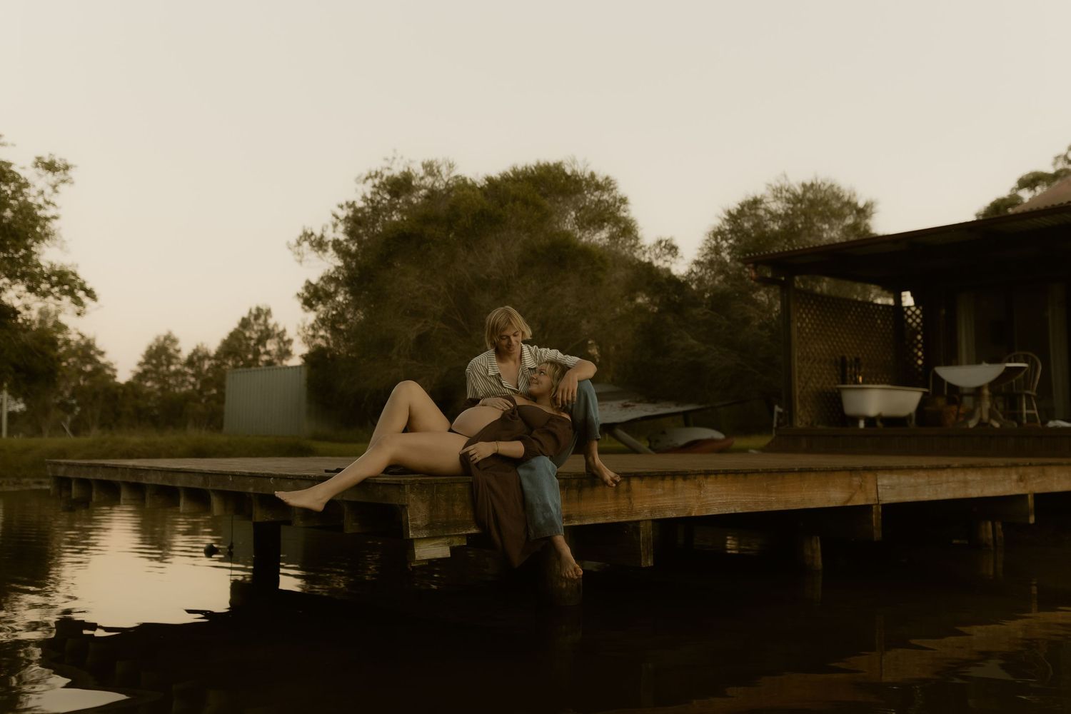 People lounging on a wooden dock by the water during golden hour.