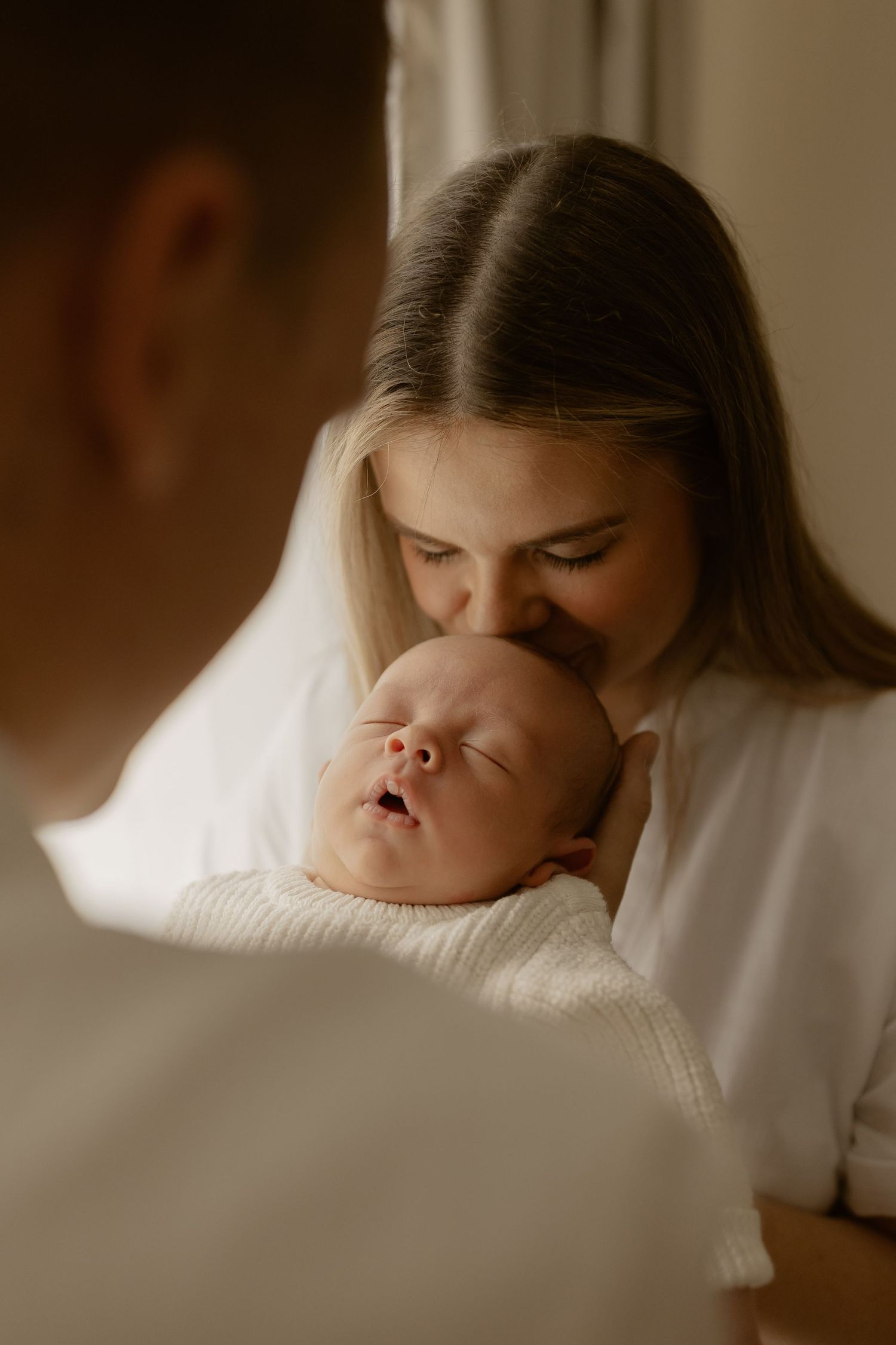 Intimate portrait capturing tender moment with sleeping newborn in warm lighting.