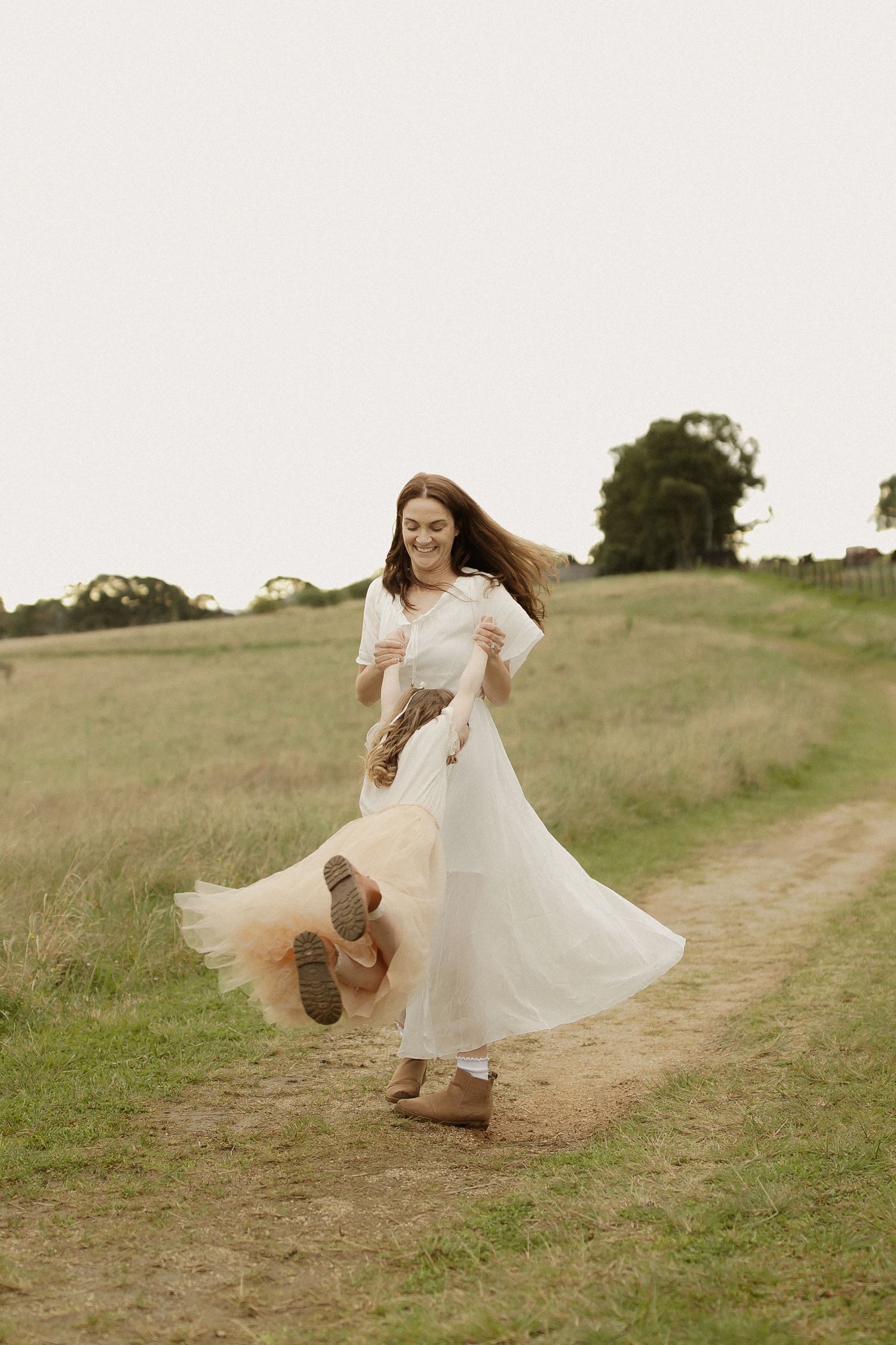 A playful photo sequence of someone twirling in a white dress and cowboy boots on a dirt path in a grassy field.
