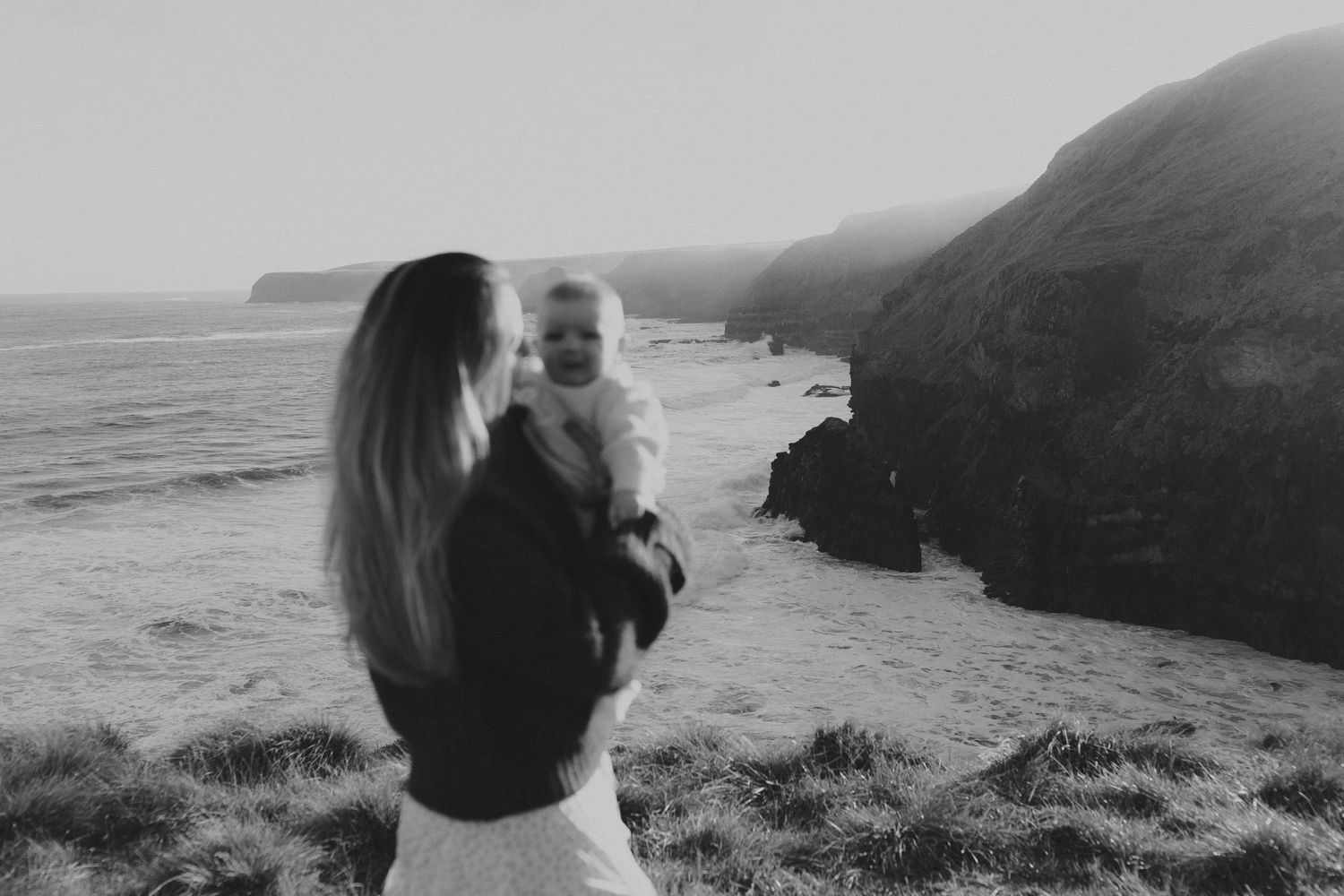 Black and white photo of mother holding baby on coastal cliffs.