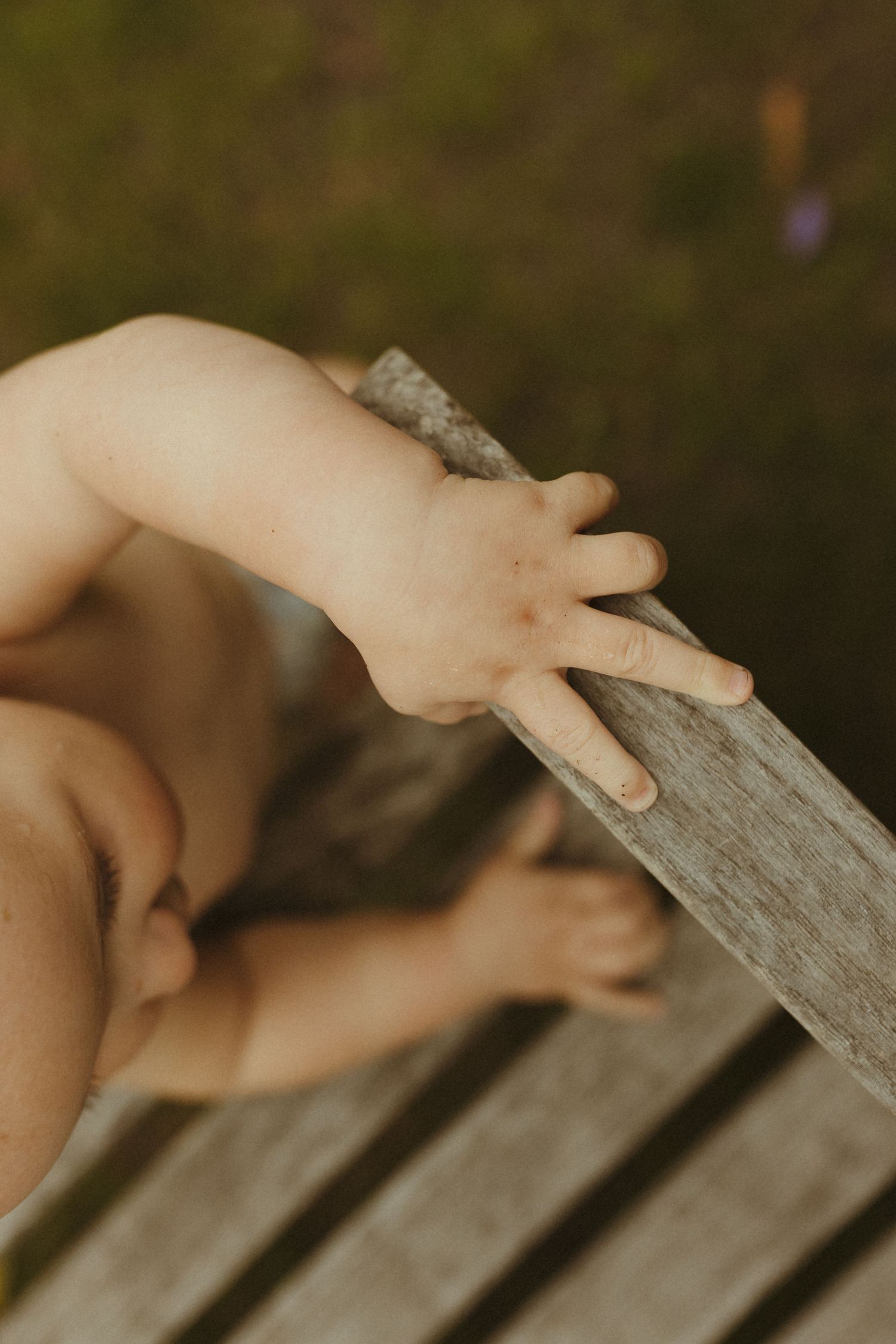 Close-up view of small fingers gently touching weathered wooden slats in natural lighting.
