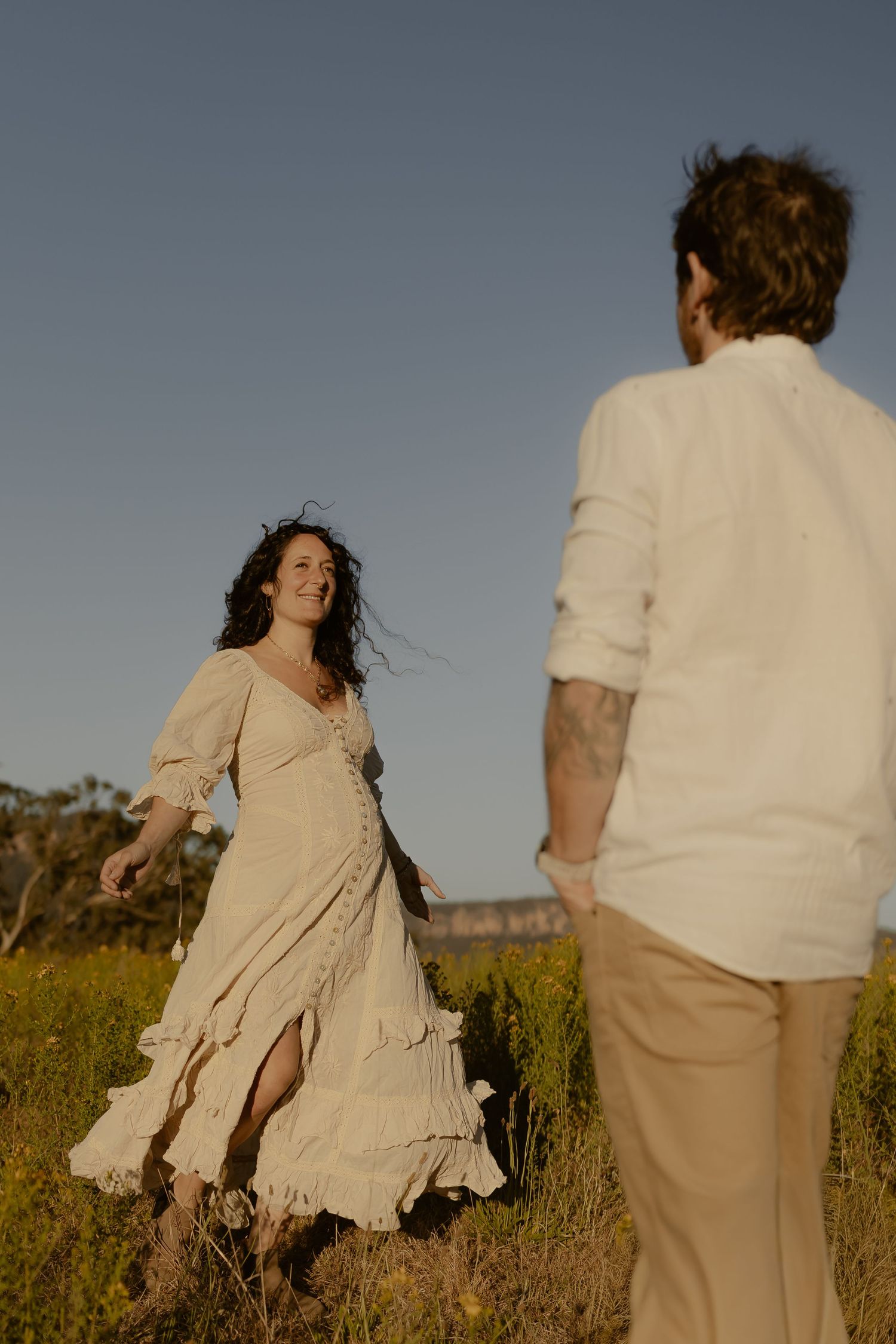 Two people dance and twirl through a wild meadow with mountains visible in the background.