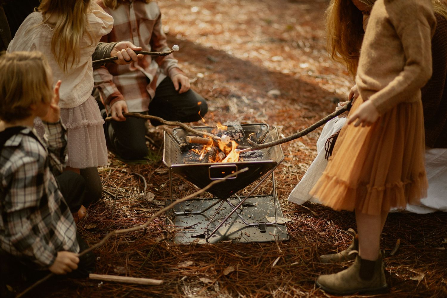 Intimate family gathering around a warm campfire in the woods with fallen autumn leaves.