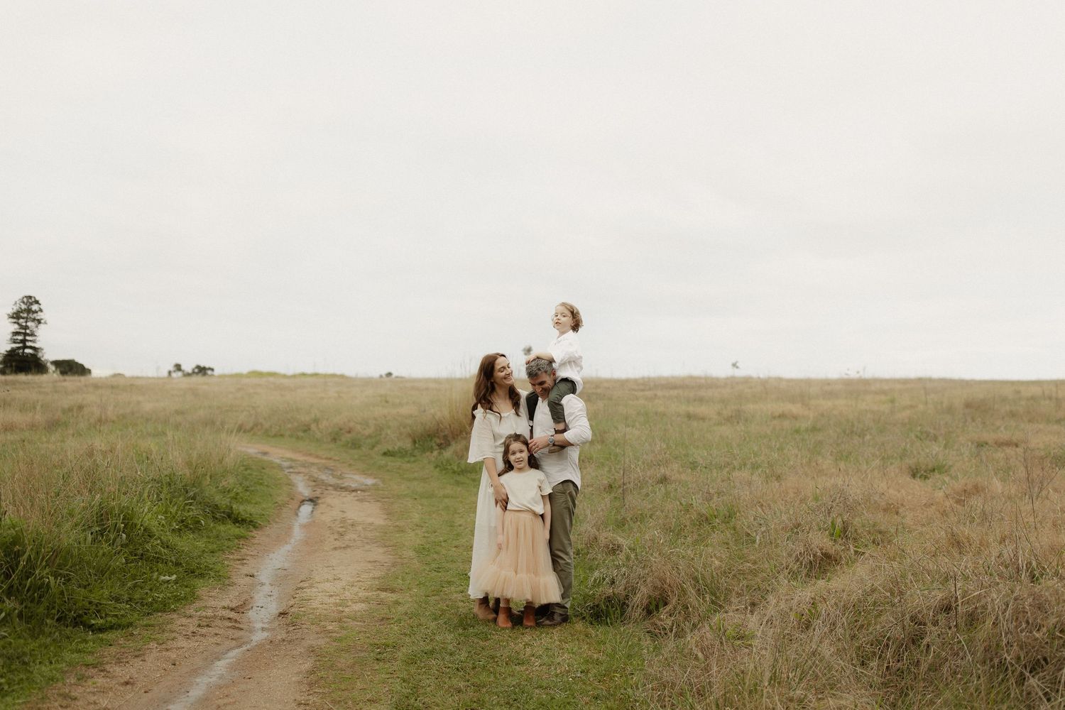 A couple walks hand in hand through a golden grass field during sunset on a hilltop path.