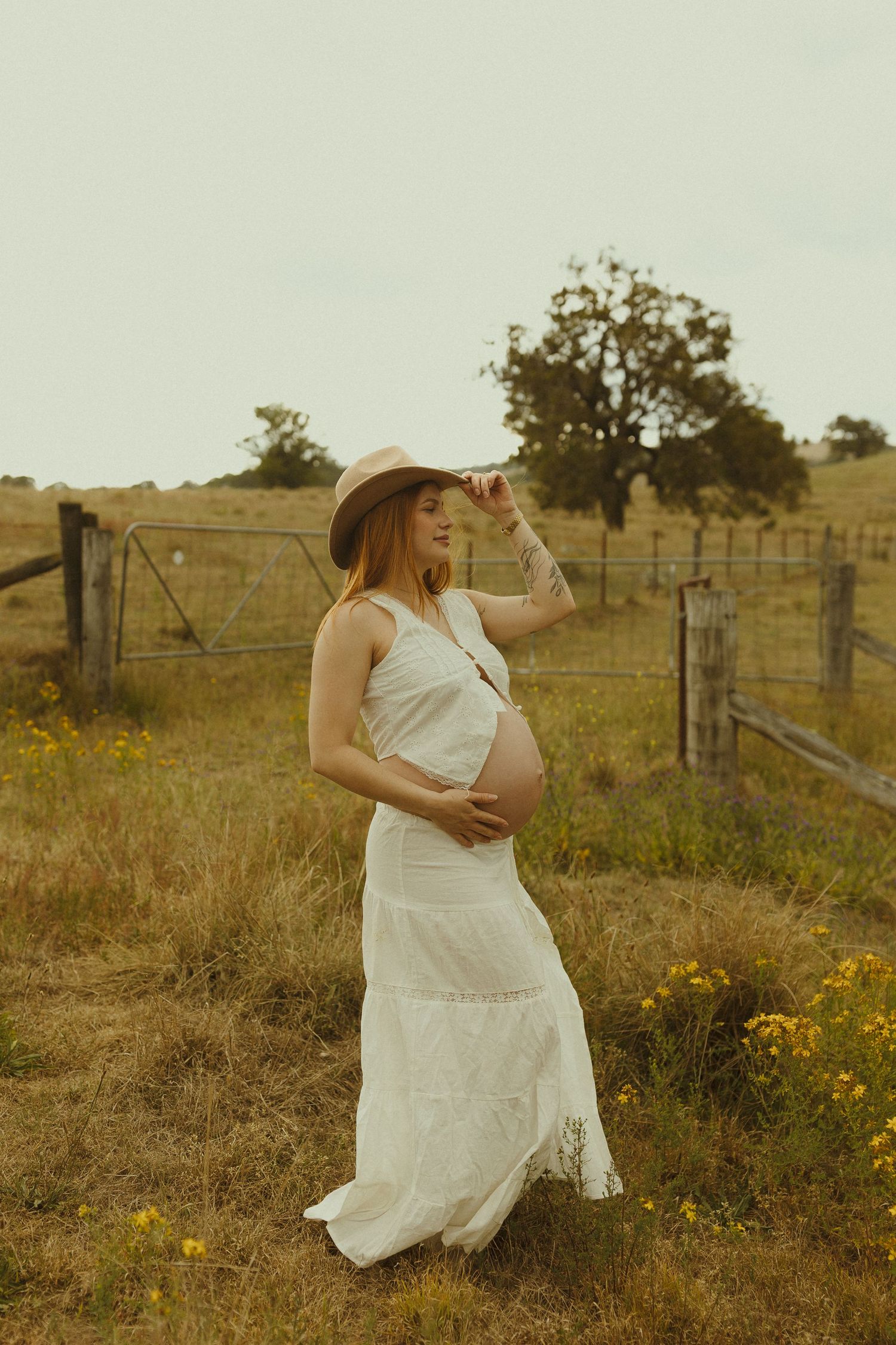A sun-washed portrait of someone in a white dress standing by an old wooden fence in golden afternoon light.