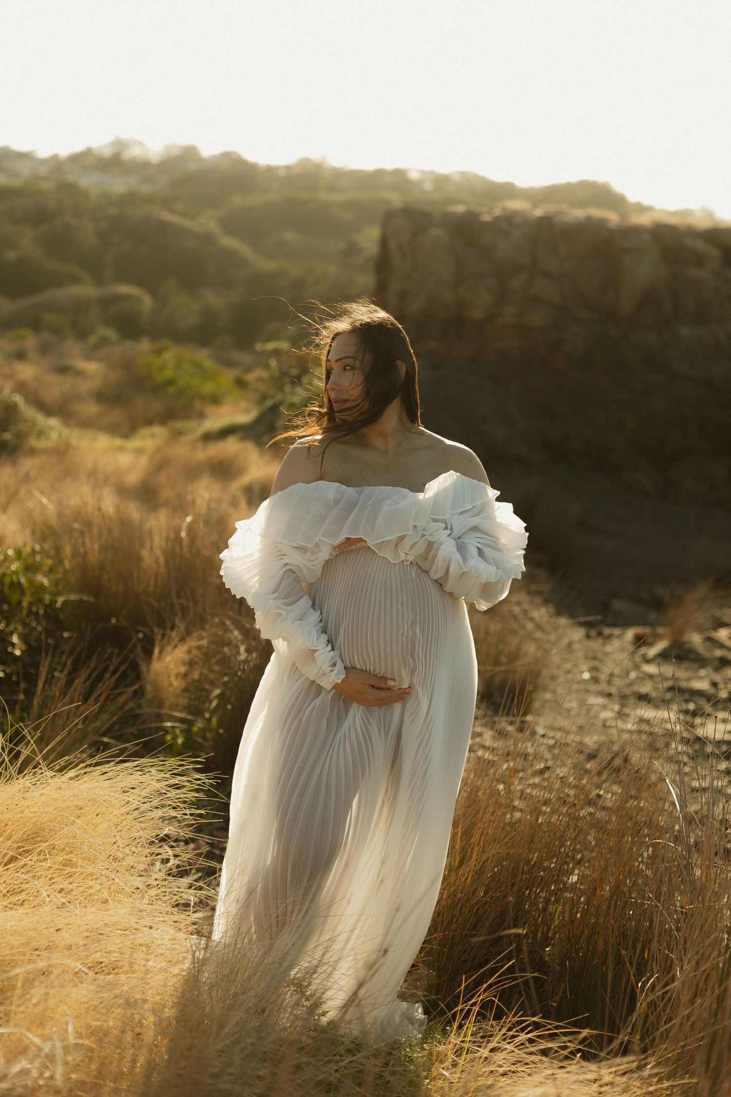 Two figures in flowing white dresses share an embrace in golden evening light.