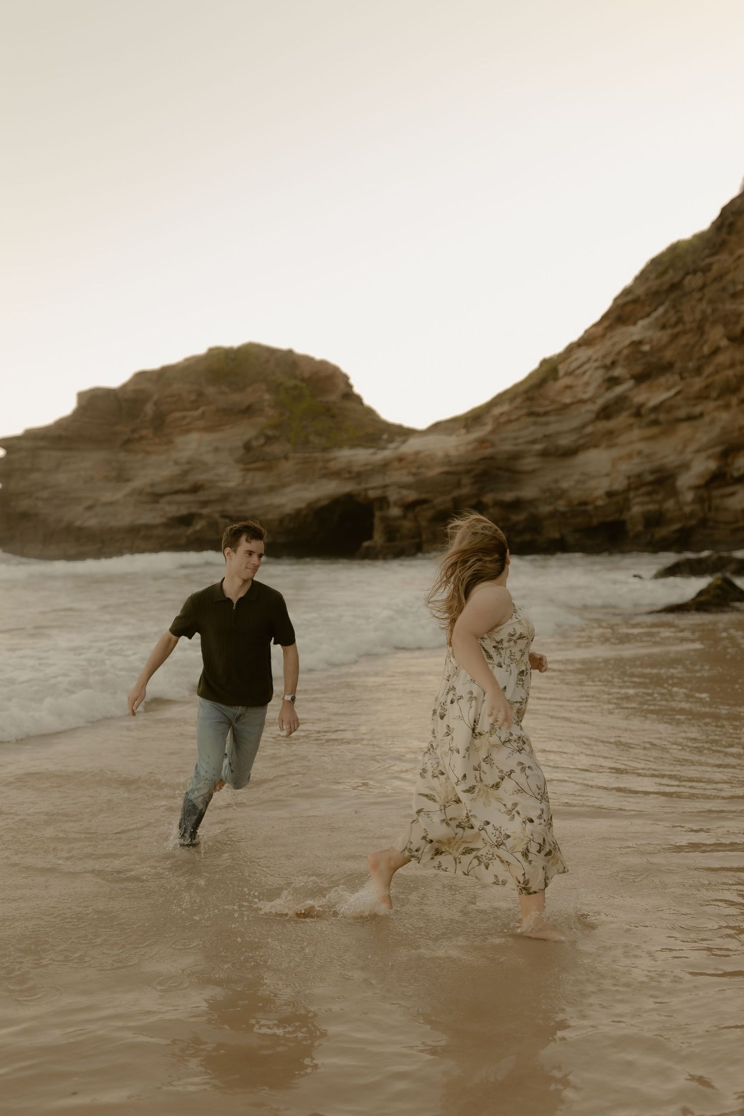 Couple playfully running and splashing through shallow ocean waves at the beach.