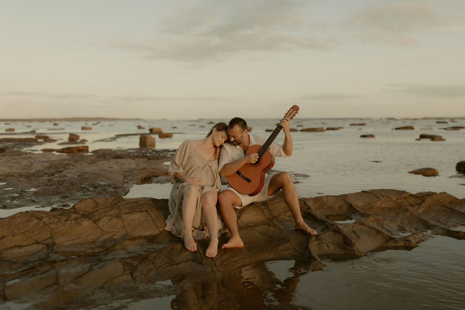People sit on rocky coastal shore at sunset enjoying peaceful ocean views and atmosphere.