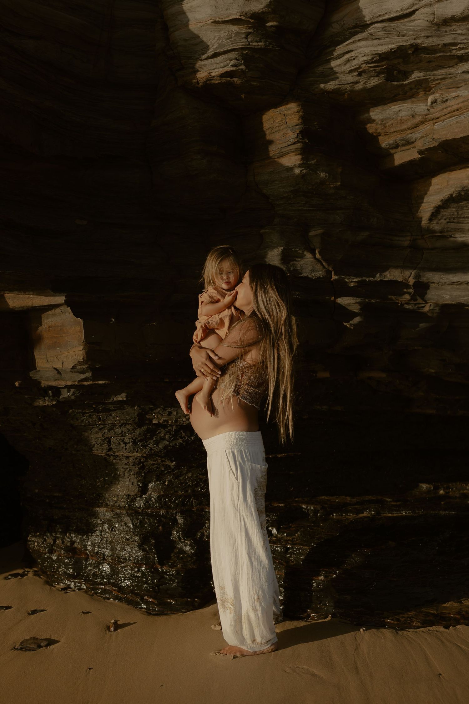 A tender embrace captured against a rocky cave wall backdrop in soft lighting.