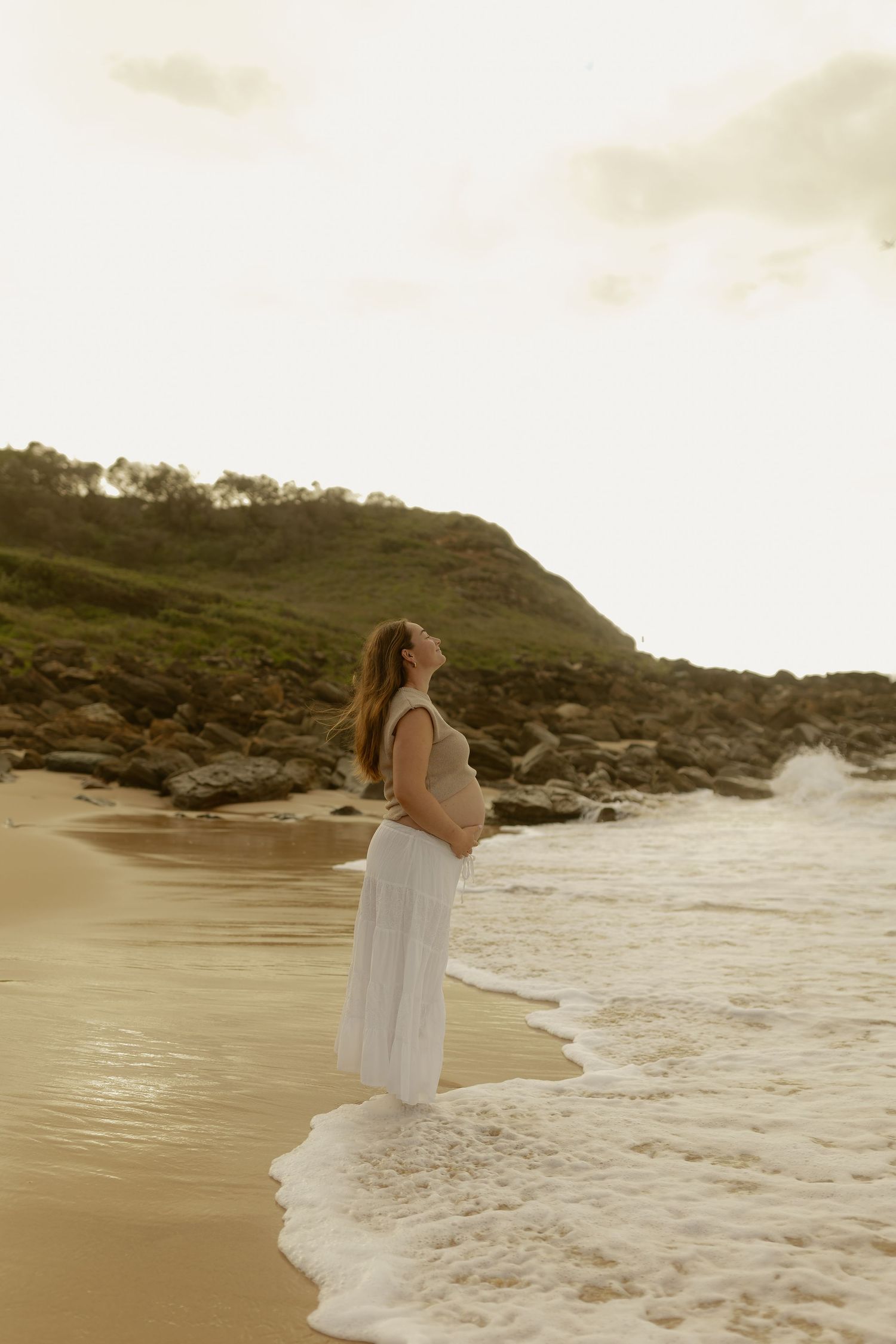A dreamy beachside scene shows a figure in white near crashing waves at sunset.