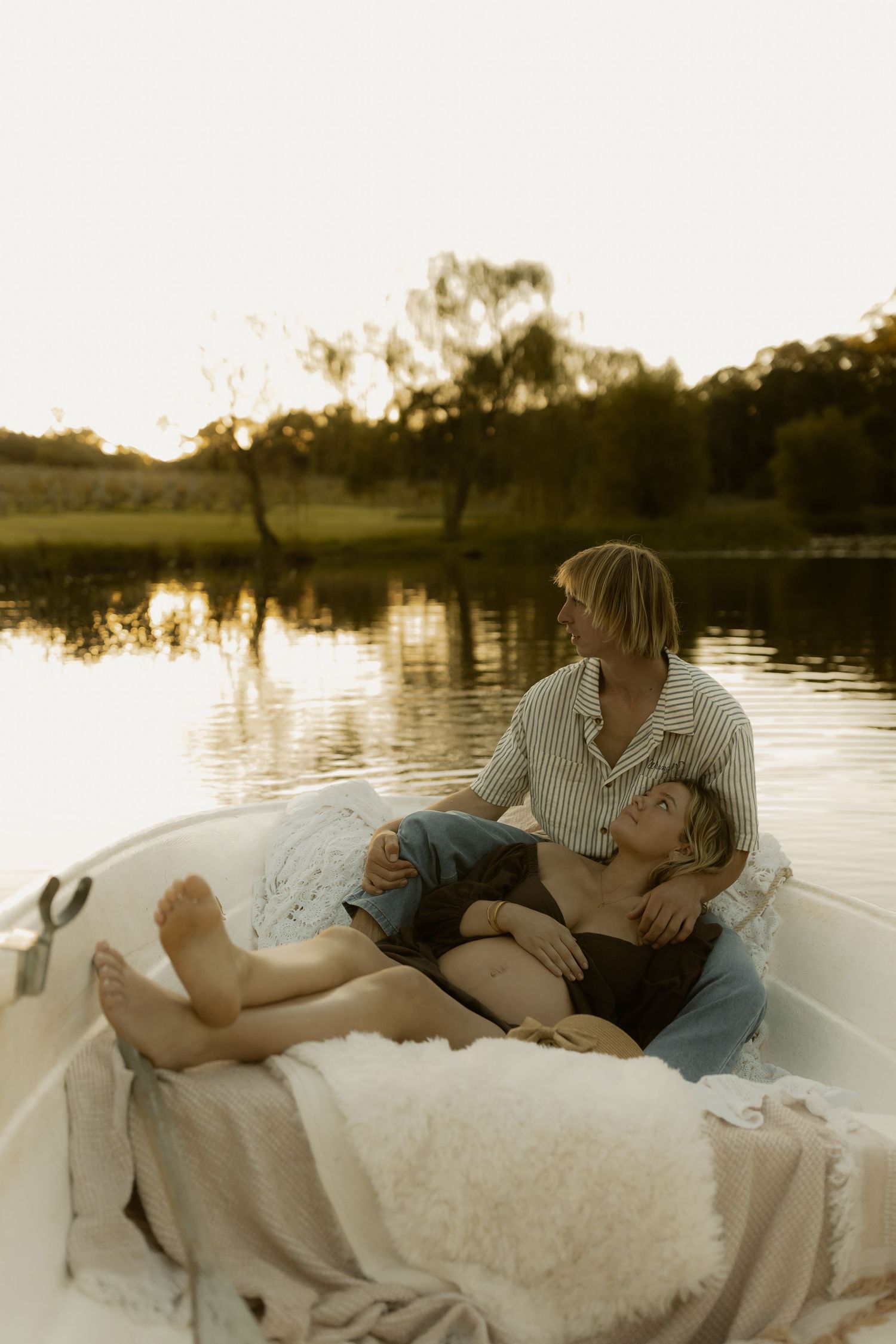 Couple relaxing on blankets in a small boat at sunset on a lake.