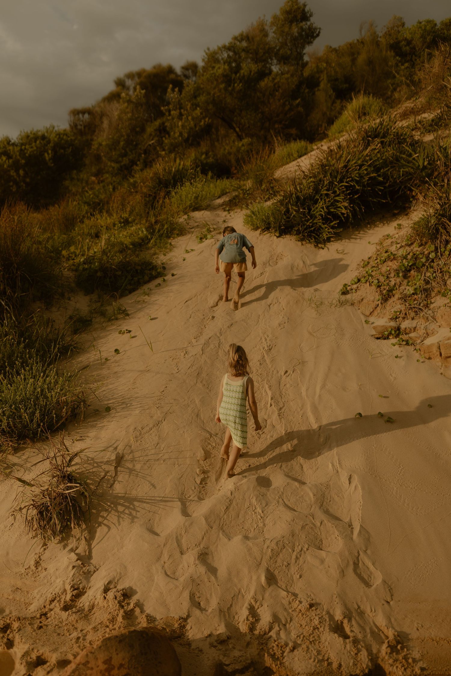 Multiple shots of people climbing and playing on golden sand dunes during sunset.