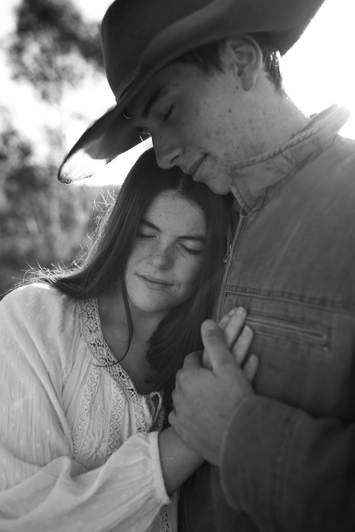 A romantic black and white portrait of a couple in western attire sharing an intimate moment.