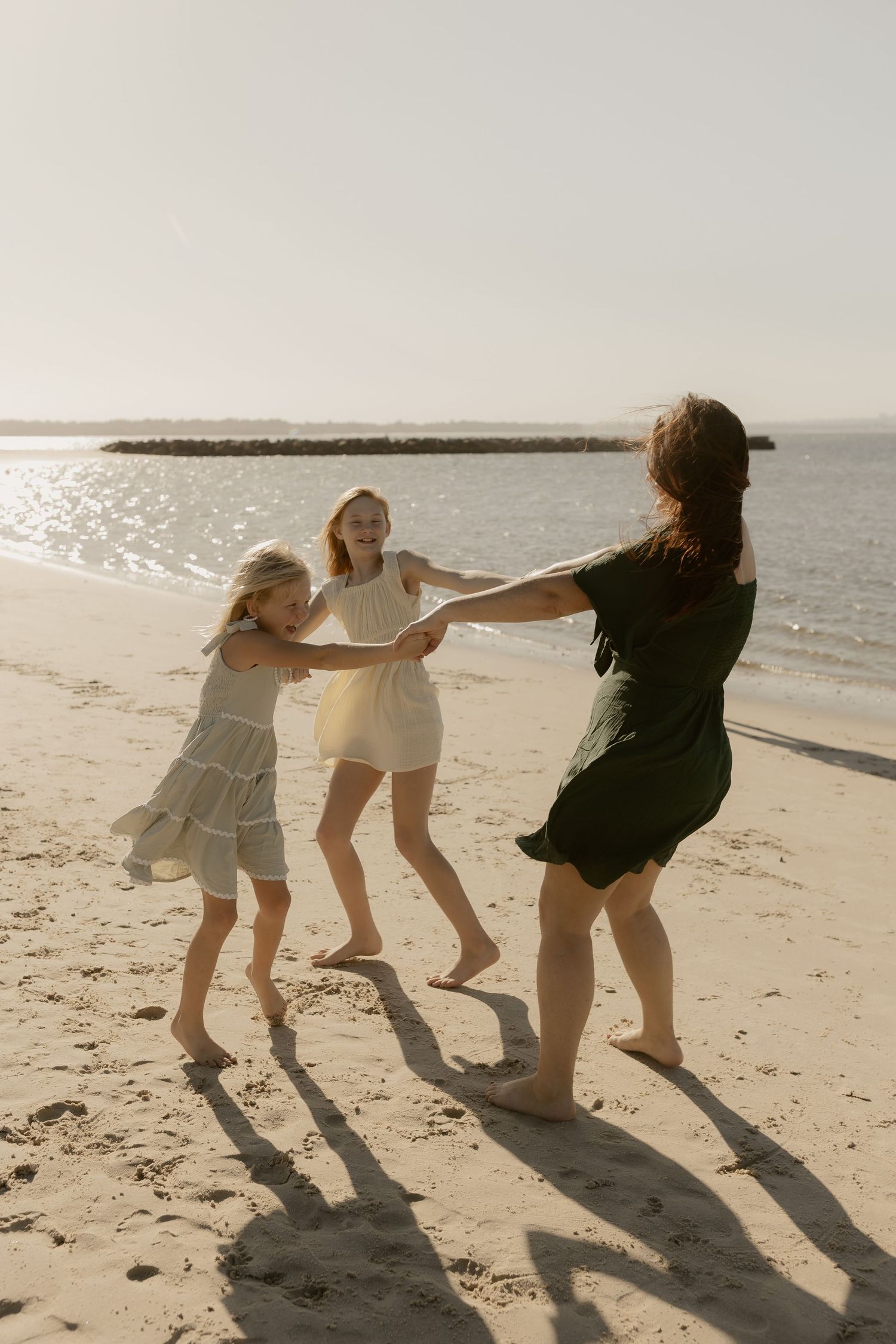 Three people hold hands in a circle, dancing together on the beach during golden hour.