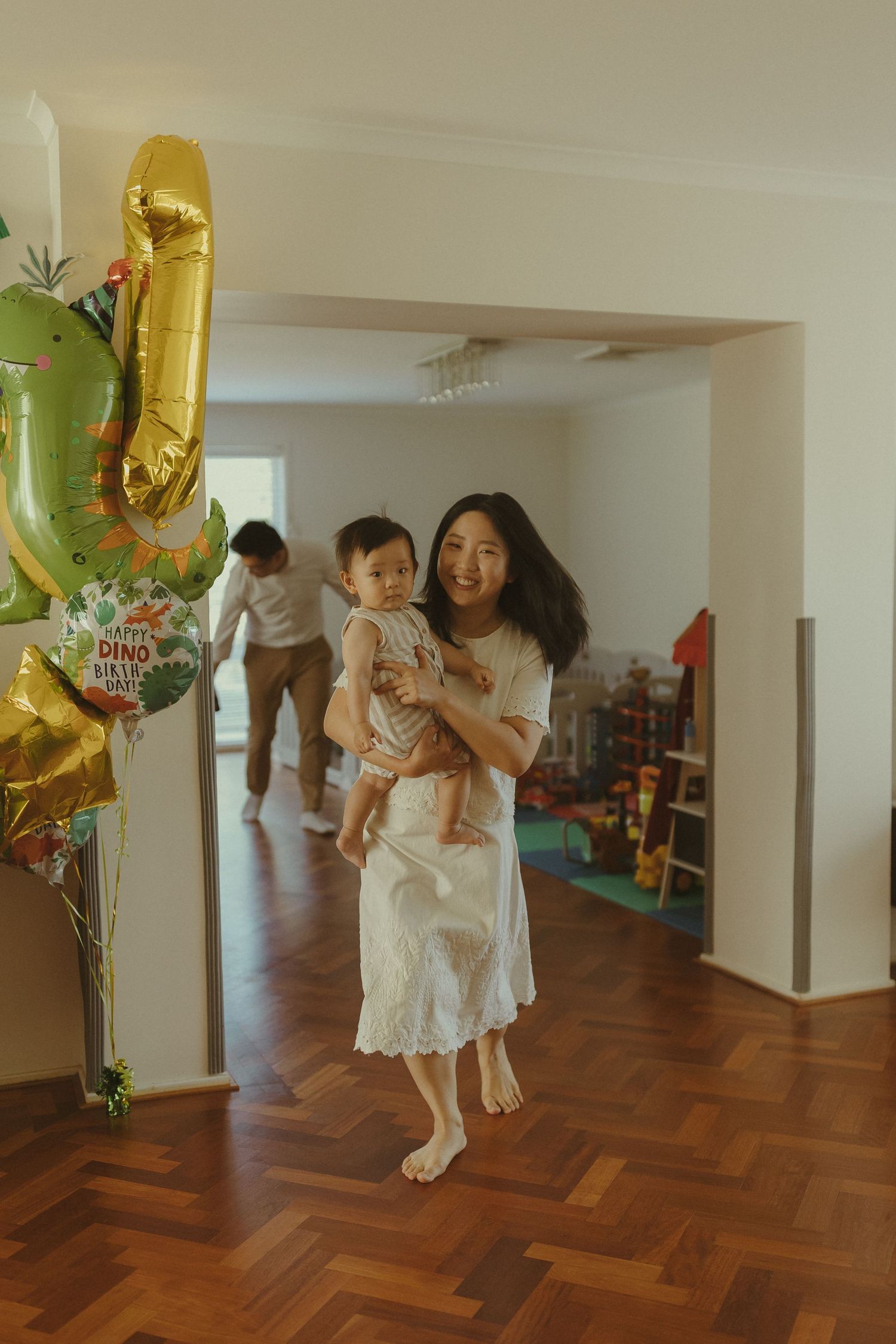 People in white outfits dance and play in a room with hardwood floors and festive decorations.
