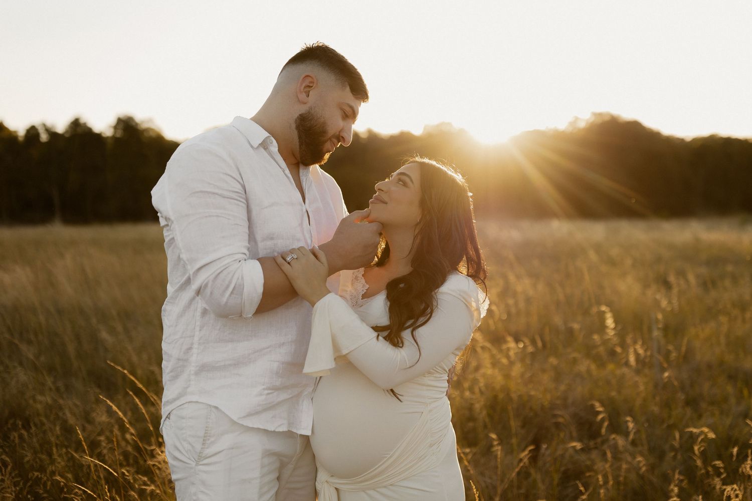 A romantic couple embraces in a golden wheat field at sunset during a dreamy engagement photoshoot.