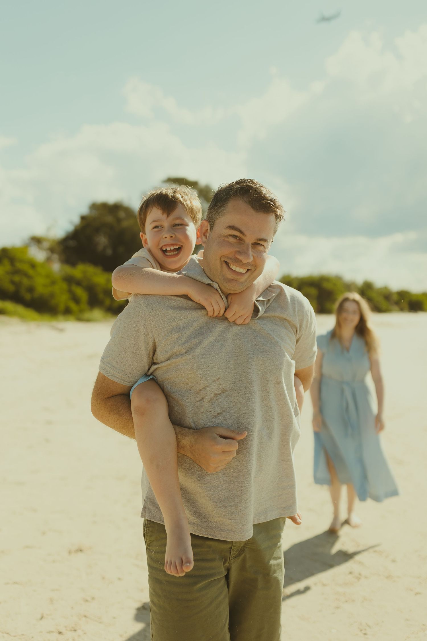 Happy family enjoying a sunny day at the beach with a piggyback ride and casual stroll along the sand.