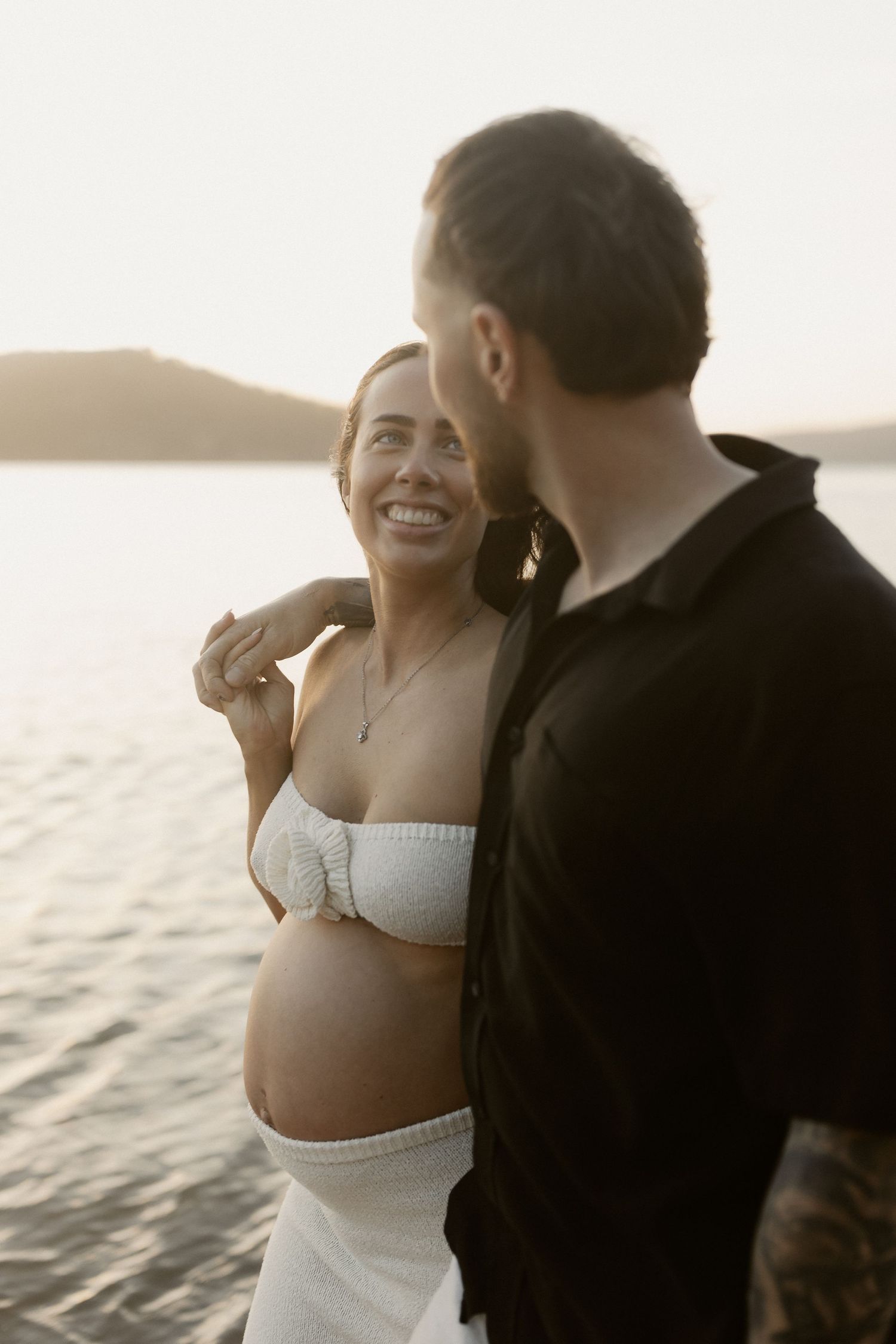 Romantic series of beach engagement photos showing couple embracing at sunset by the ocean waves.