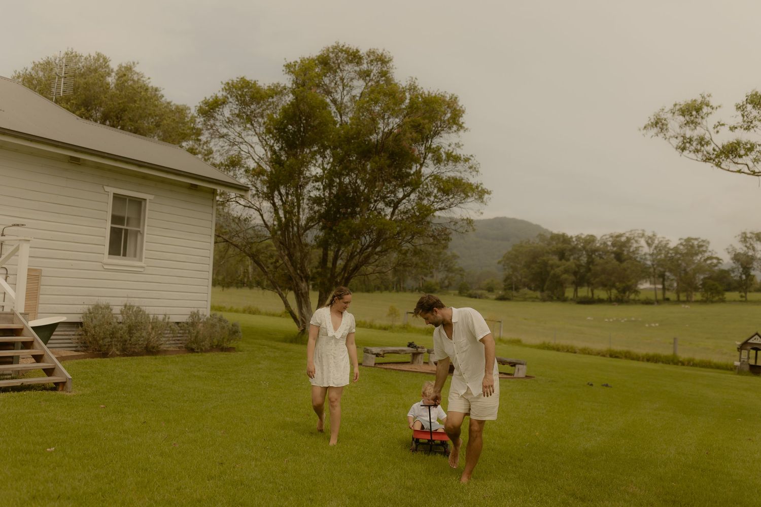 Rural landscape showing family activities near a white farmhouse.