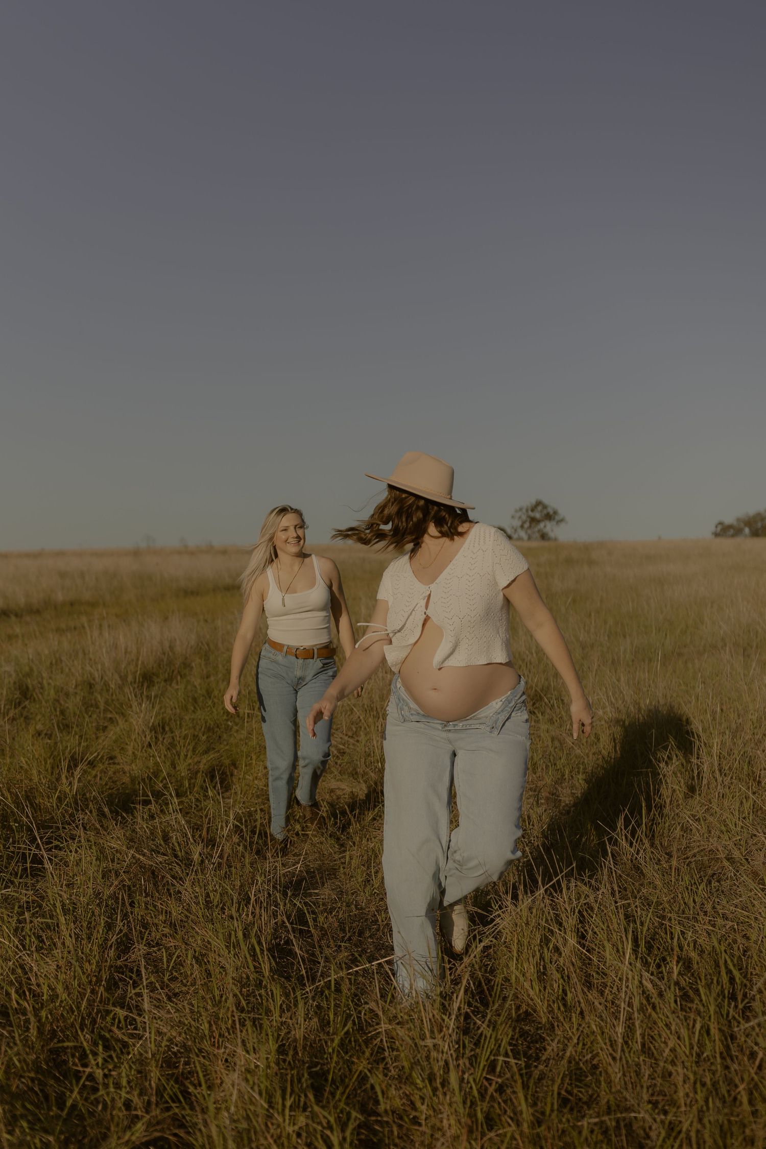 Two figures walk together through a sun-drenched field of tall grass at golden hour.
