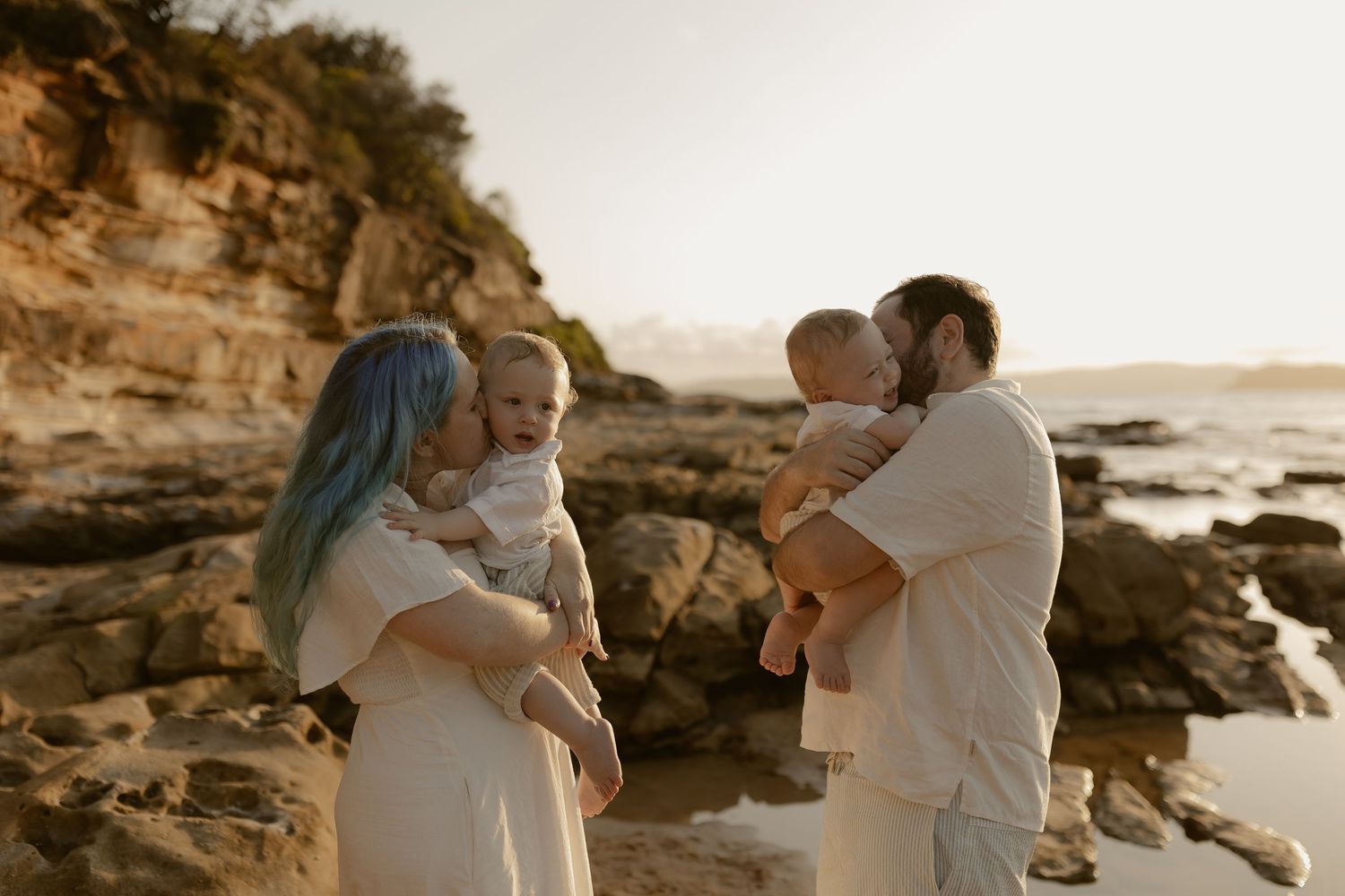 Family enjoying tender moments together on a rocky beach at sunset.