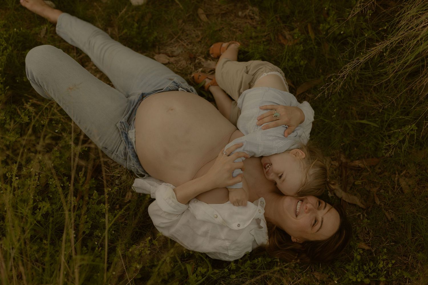 Someone lies on grass wearing a white top and light denim jeans in a dreamy outdoor setting.