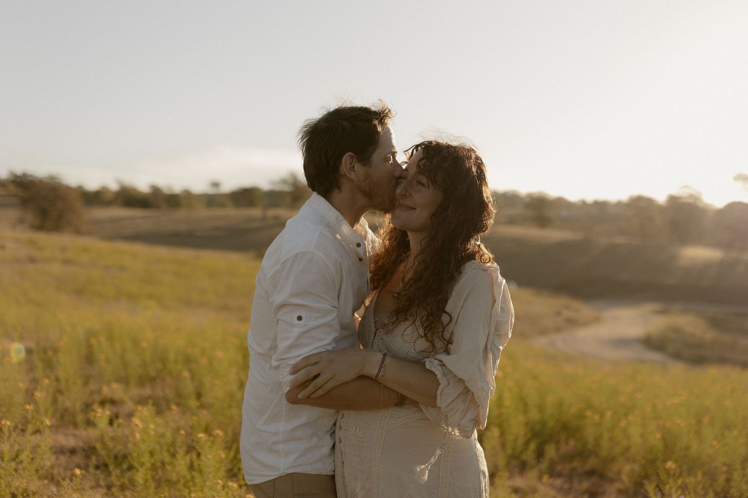 Couple sharing tender embrace in sun-drenched field during golden hour.