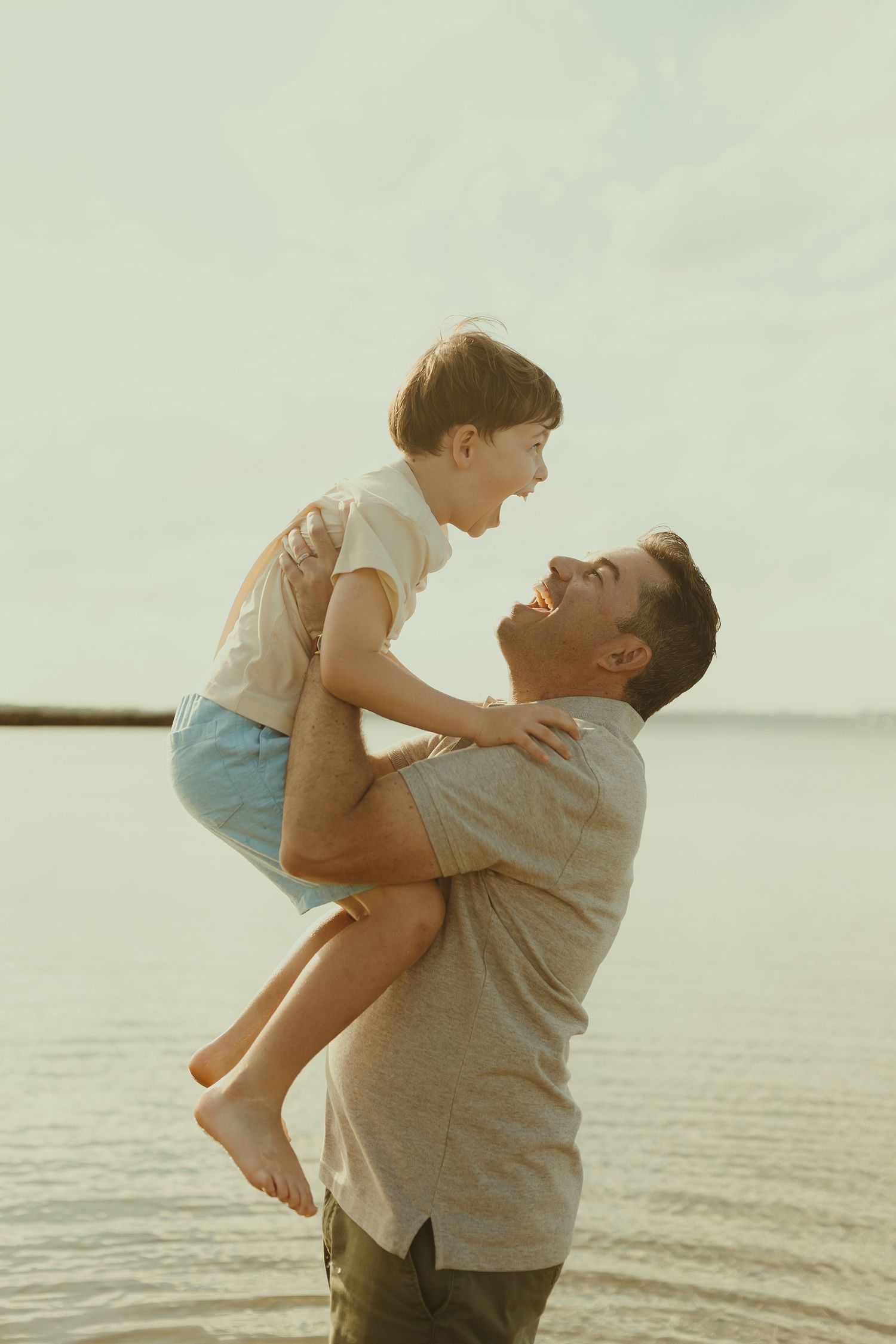 Parent and child sharing a playful moment together by the ocean at sunset.