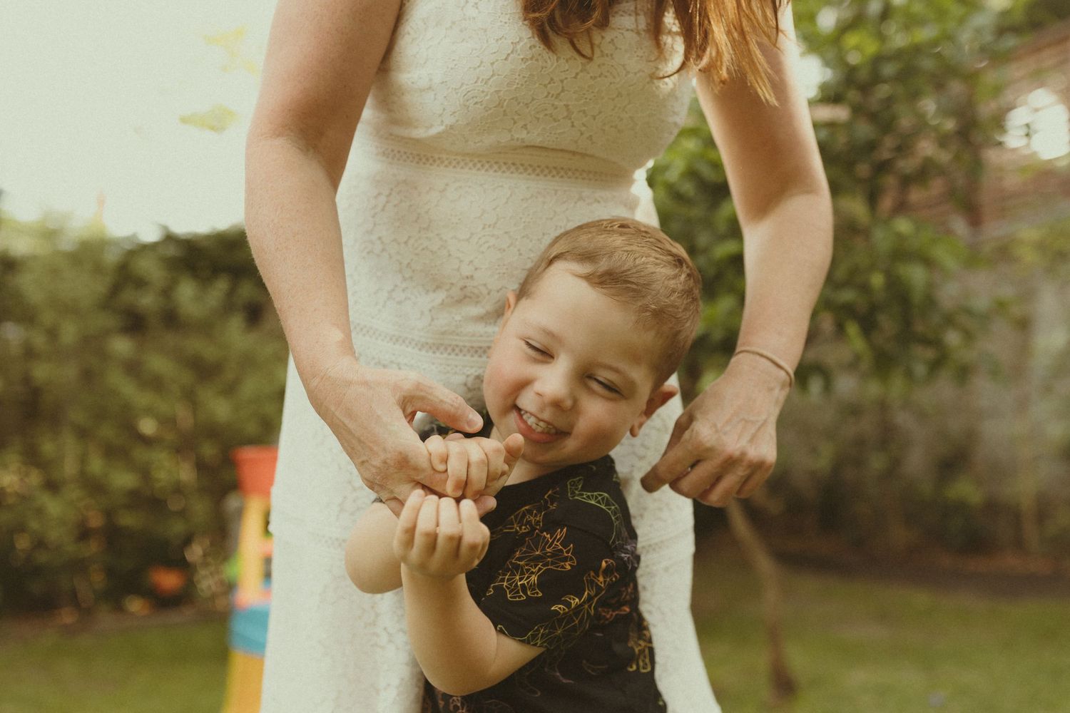 Tender family moment captured in warm sunlight against a garden backdrop.