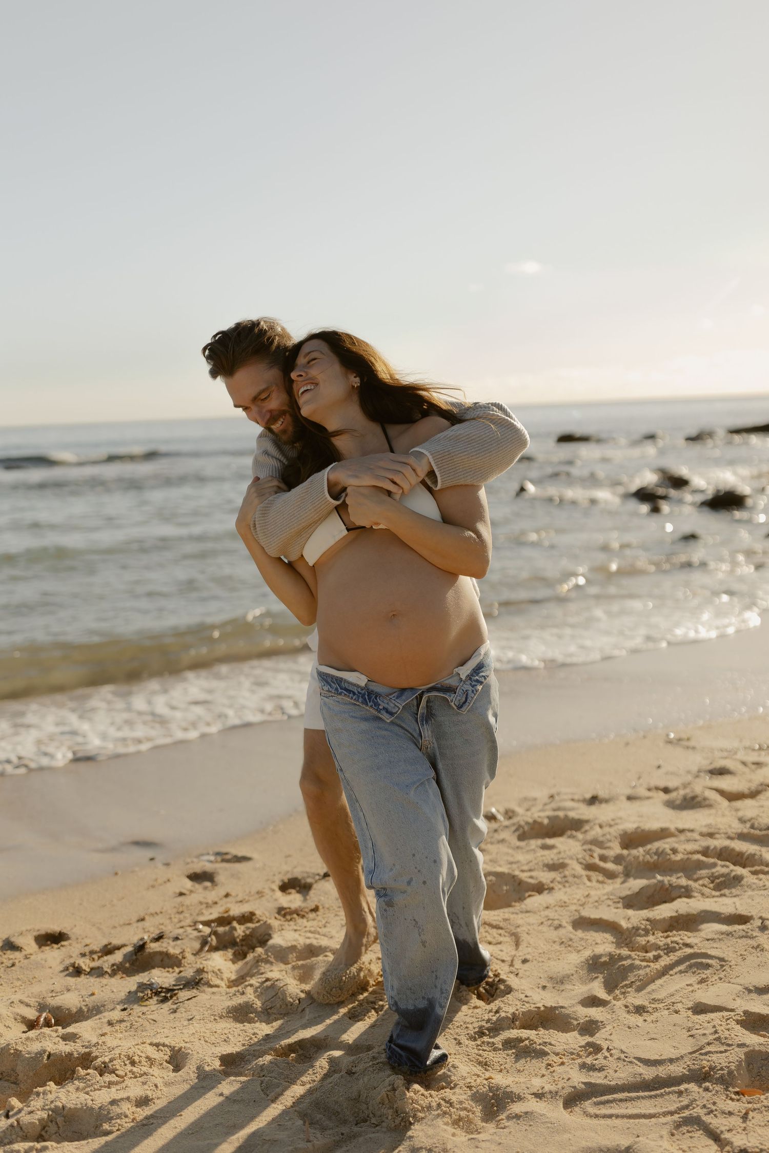 Romantic couple embracing and playing on a sunny beach with waves in the background.