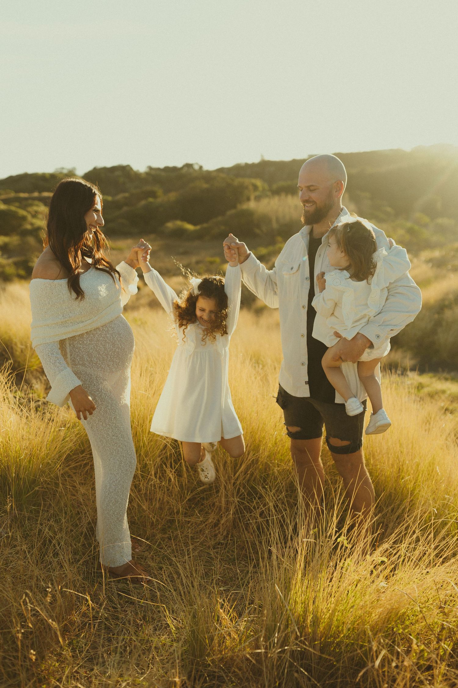 Family enjoying a playful moment together in golden sunlit grass field at sunset.