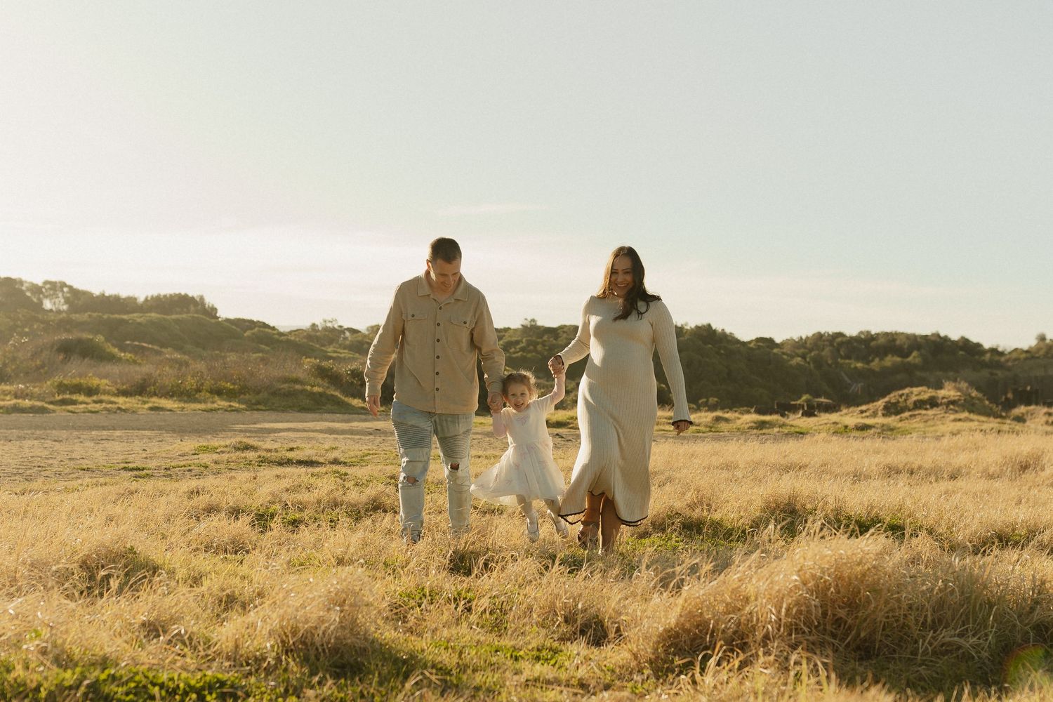 Family walking with dog through sunlit field during golden hour.
