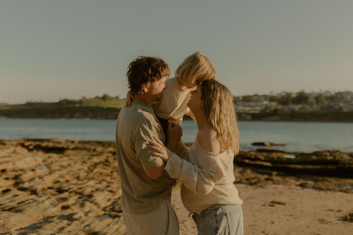 Couple sharing a tender moment with their young child on a sunlit beach.