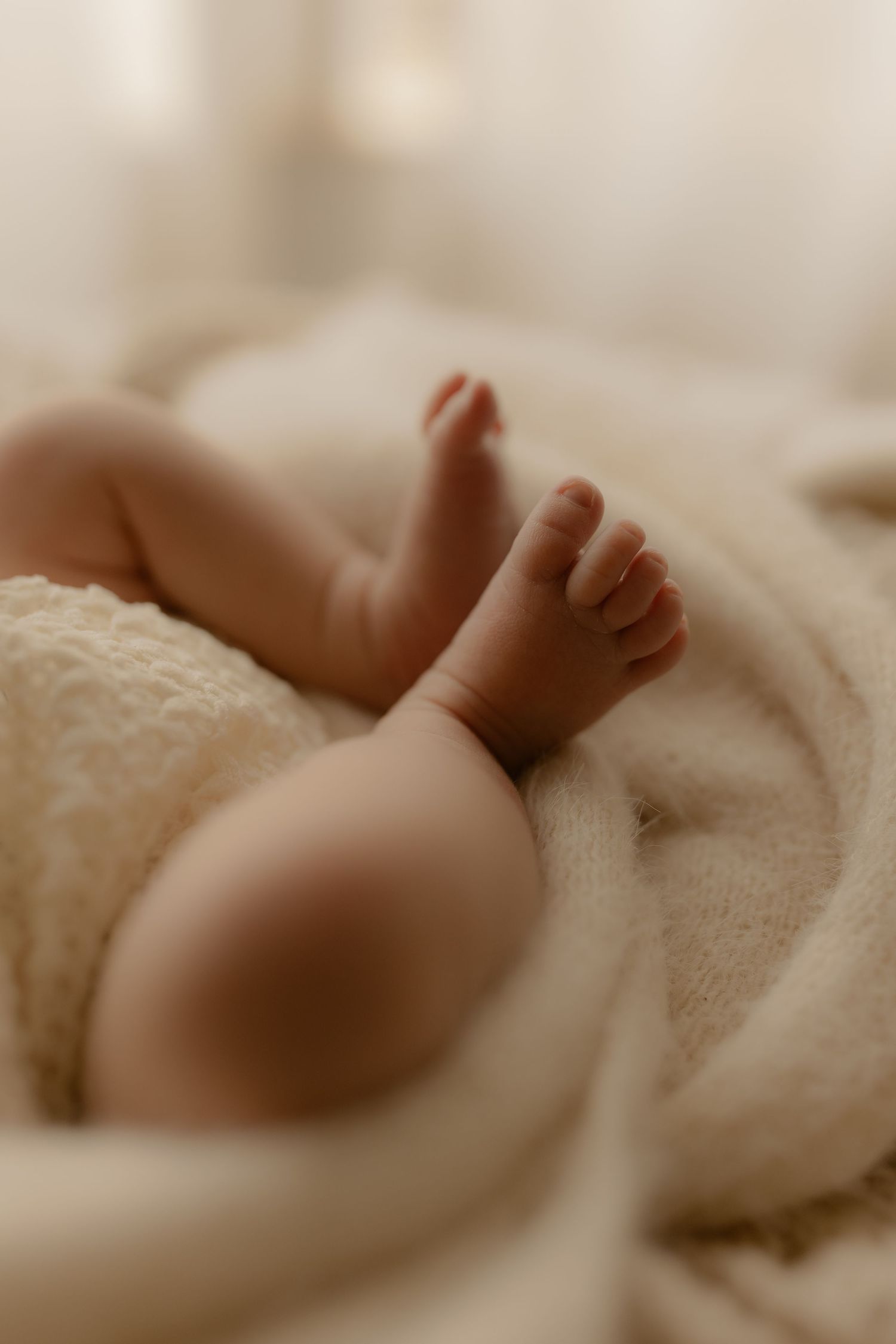 Tiny baby feet wrapped in soft white blankets in a gentle sepia tone.