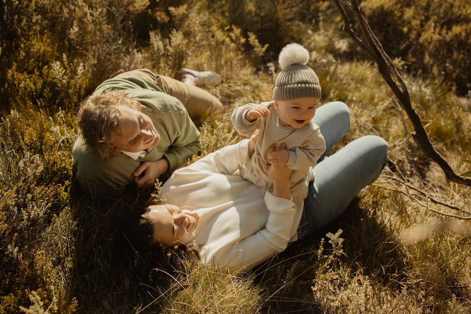 A family relaxes together on a grassy hillside during a warm autumn day.