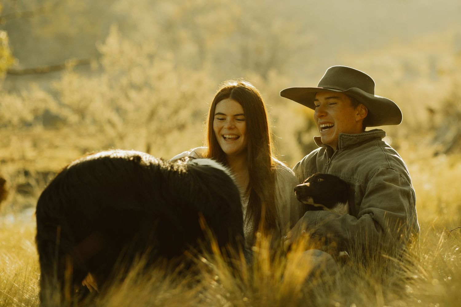 Couple sitting together in golden sunlight with dog in rustic outdoor setting.
