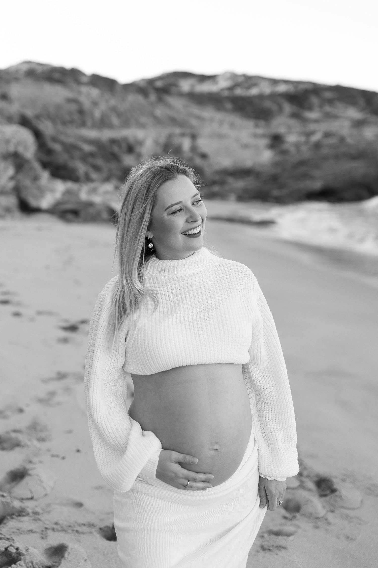 A joyful moment captured in black and white on the beach with a white sweater against coastal cliffs and sand.