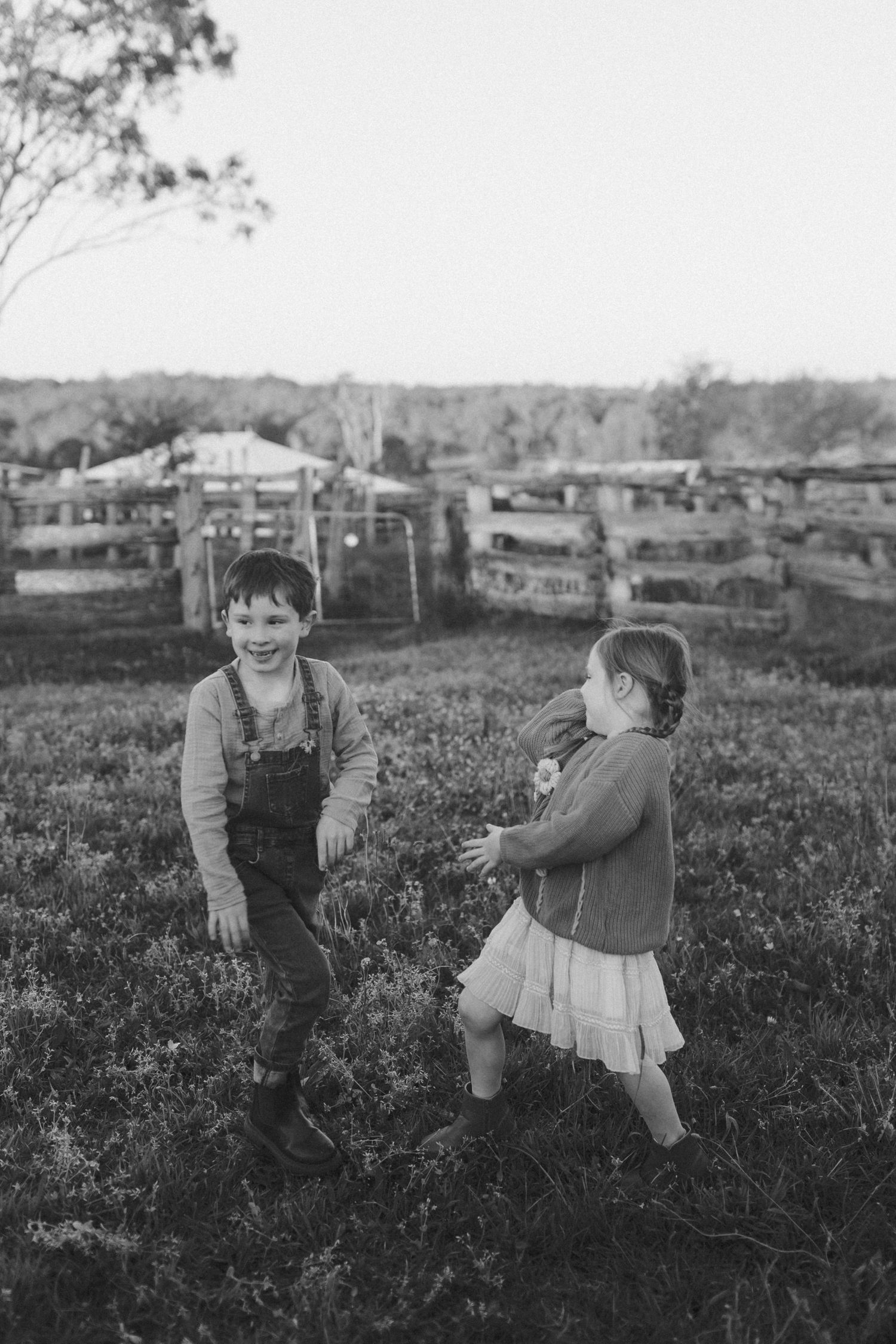 Vintage black and white photograph of children playing in a grassy field with houses in background.