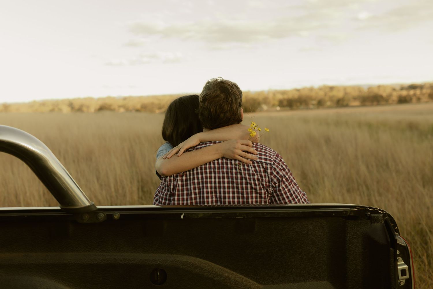 Couple embracing in truck bed overlooking golden field at sunset.