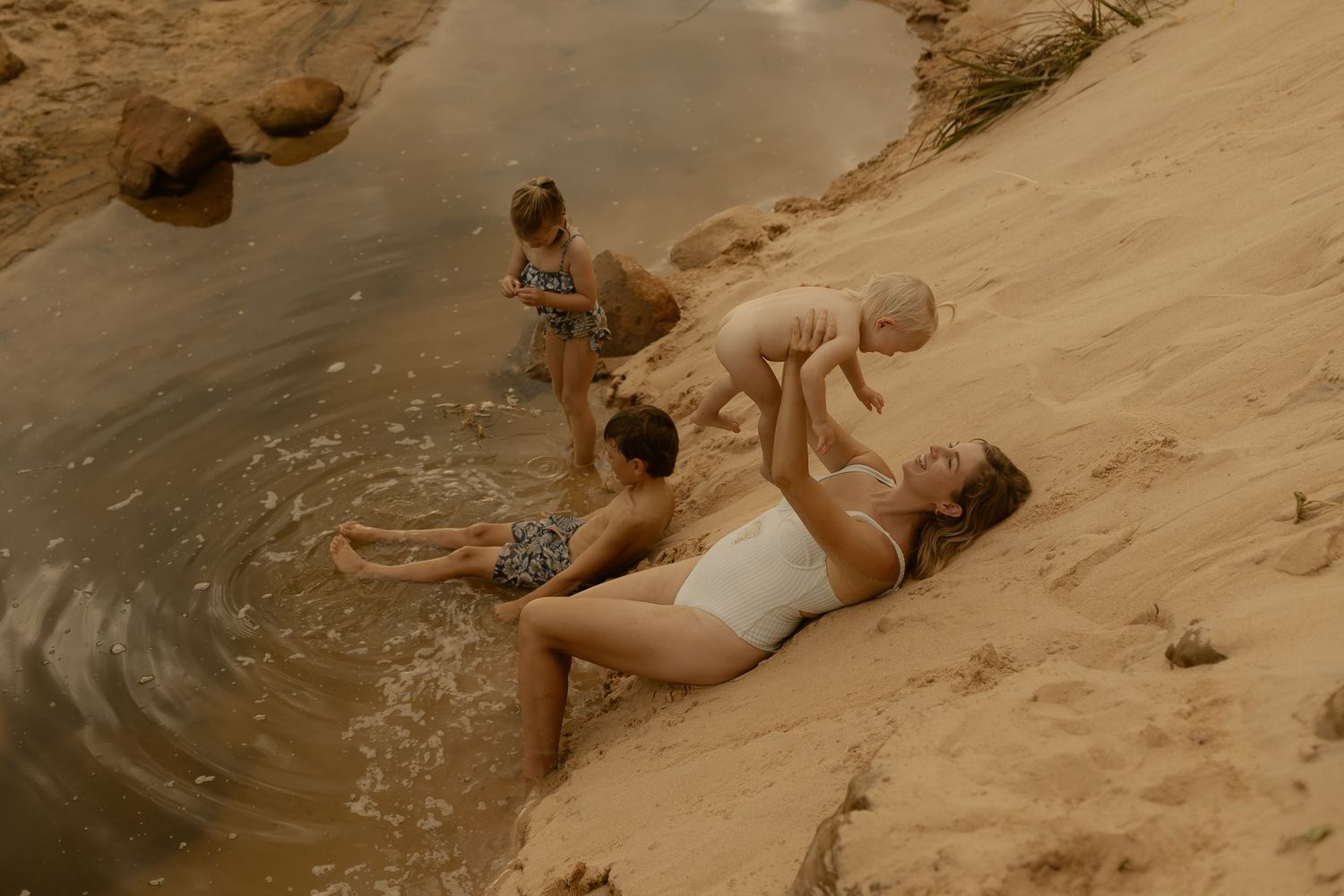 People relax and play on a sandy beach slope near the ocean waves during golden hour.
