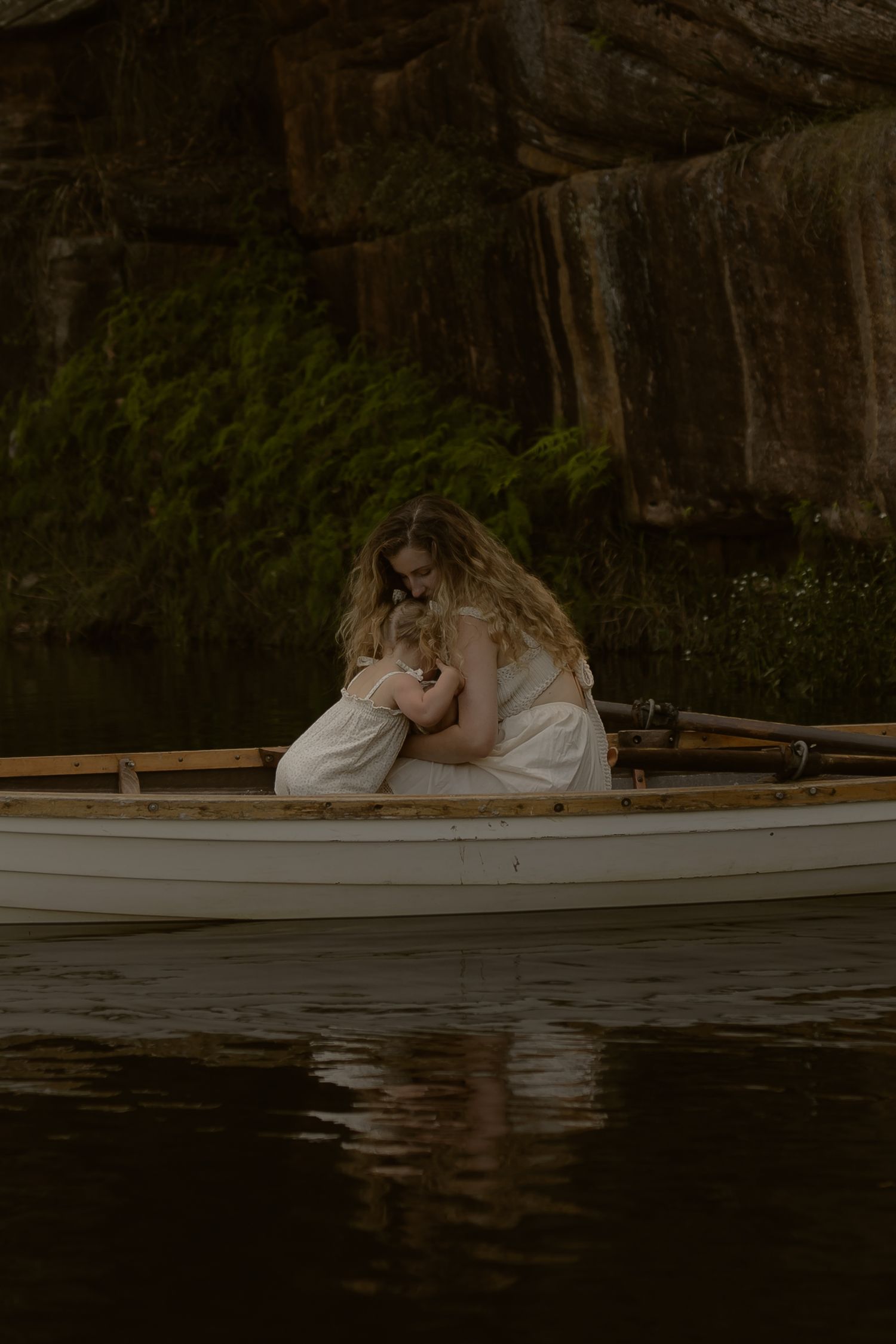 A romantic couple in white clothing embraces on a wooden dock by a tranquil lake at dusk.