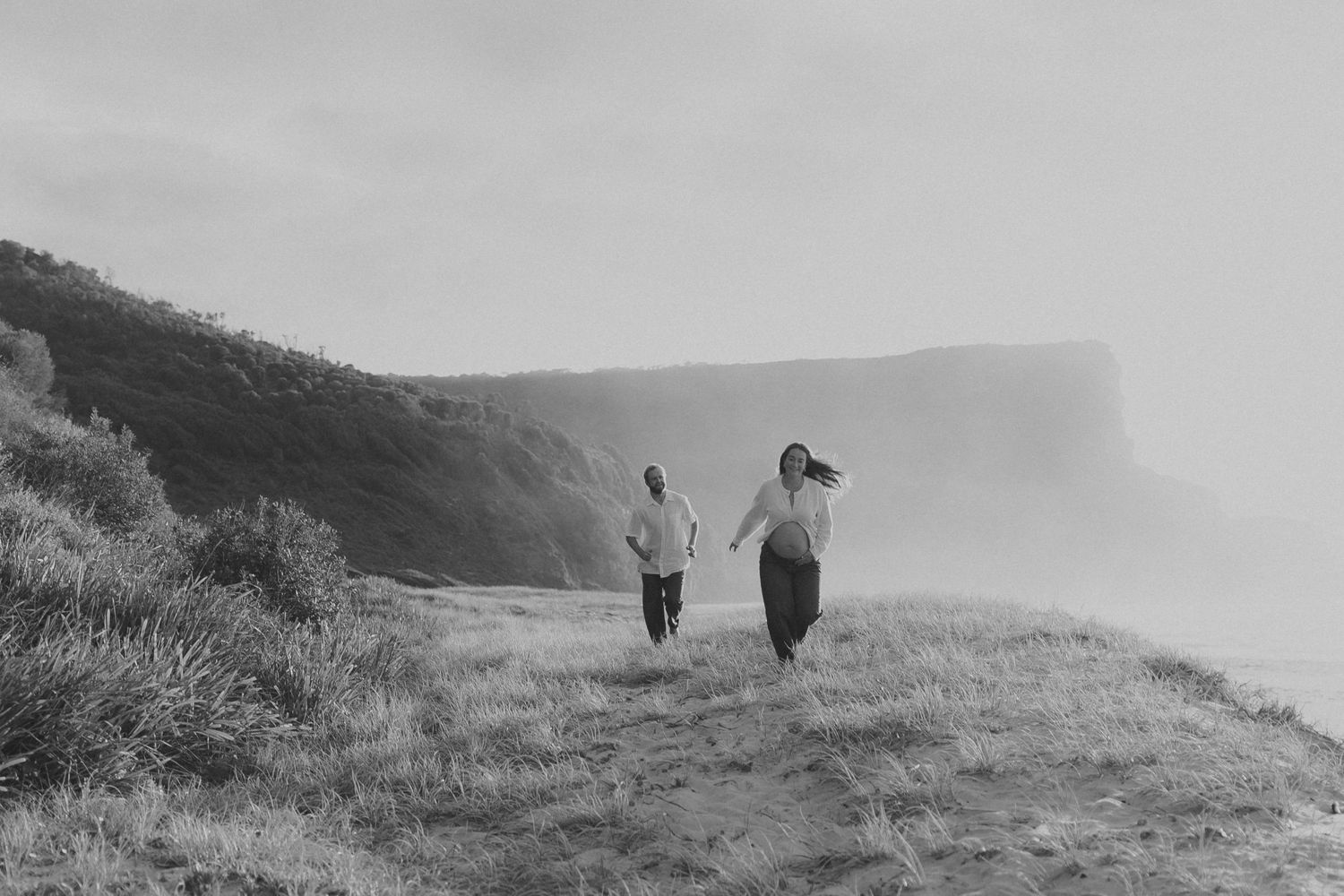 A sequence of black and white photos showing people walking along a misty coastal cliff path.