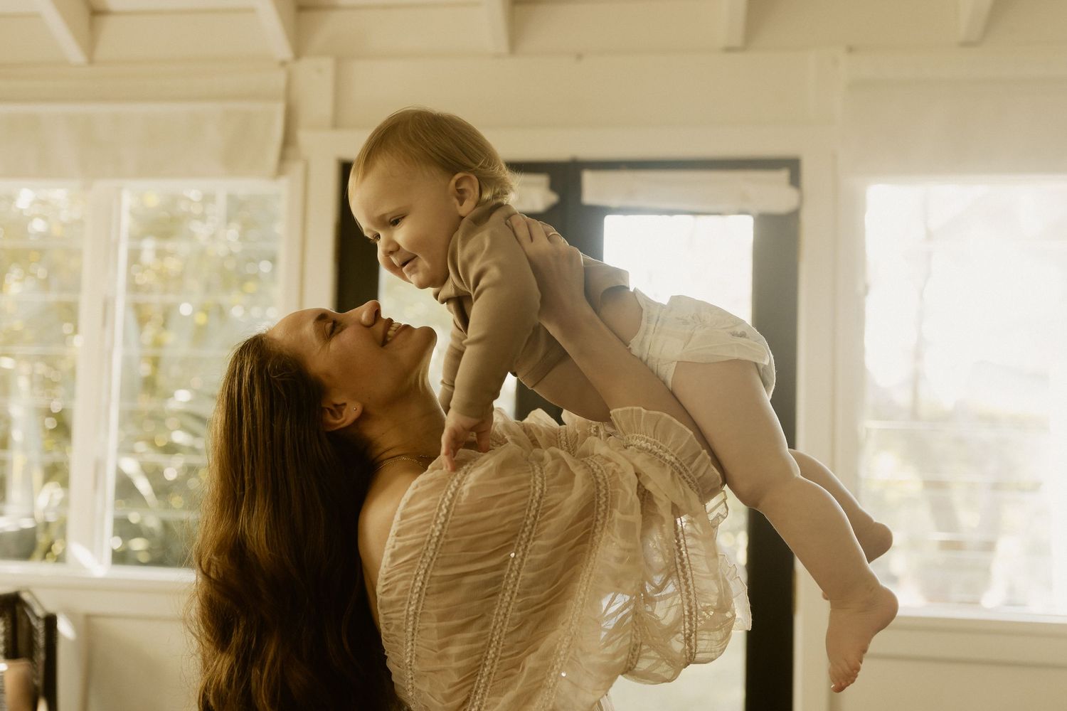 A series of four images showing a mother and baby in tender moments while standing in a sunlit room with warm decor.