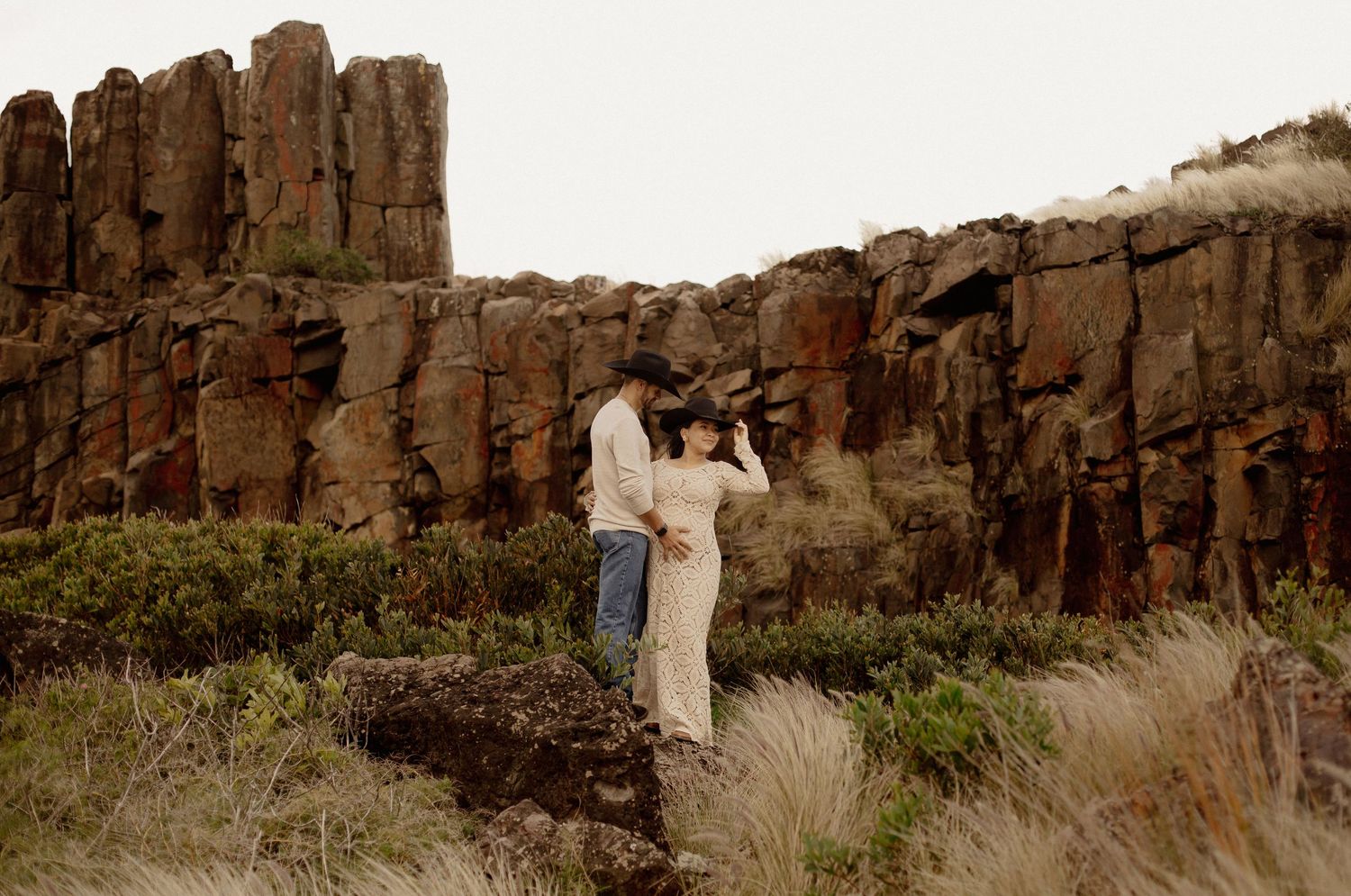 A couple shares a romantic moment against dramatic desert cliffs during their wedding photoshoot at sunset.
