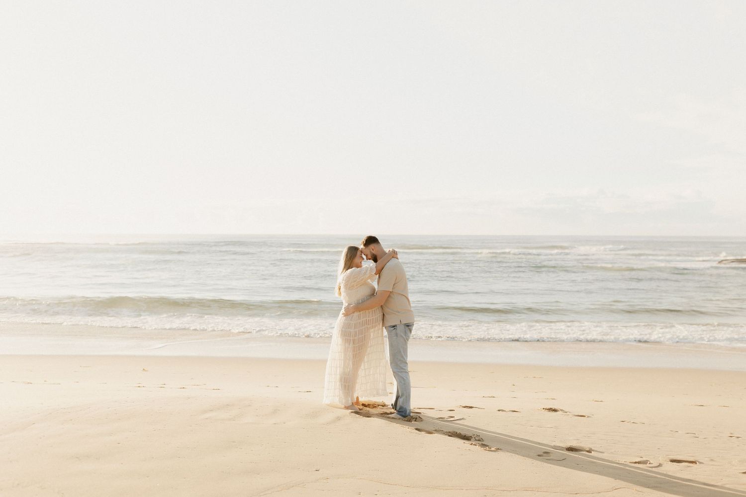 Romantic couple poses together on scenic beach with rocky coastline during golden hour.