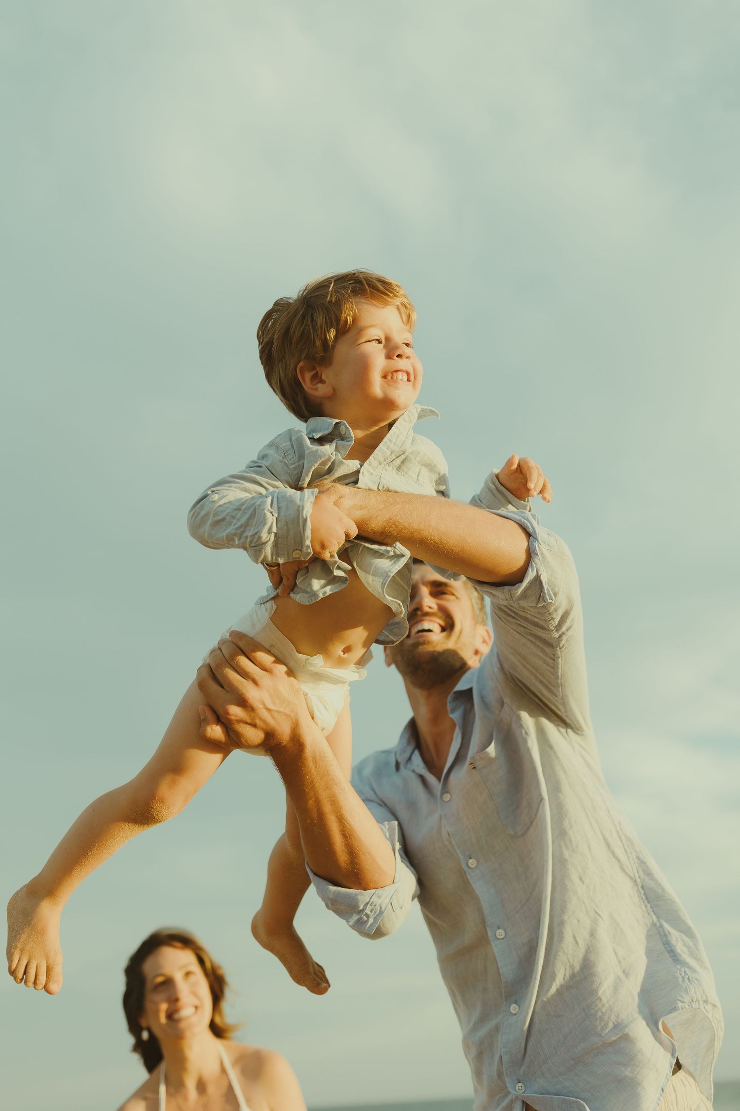 Playful moments captured of child being lifted into the air against a blue sky background.