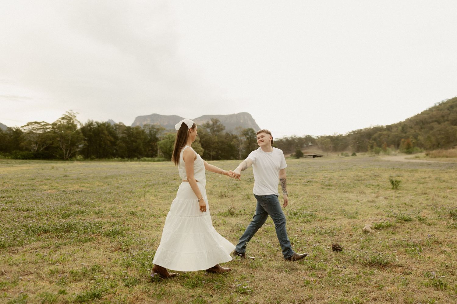 A couple dances and twirls together in a grassy meadow during a warm sunset.