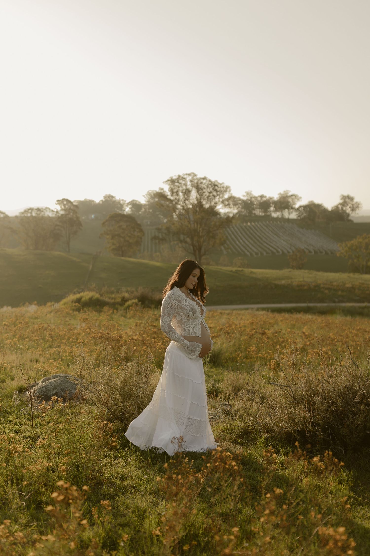 A figure in a white dress twirls through a golden wildflower meadow at sunset with rolling hills in the background.
