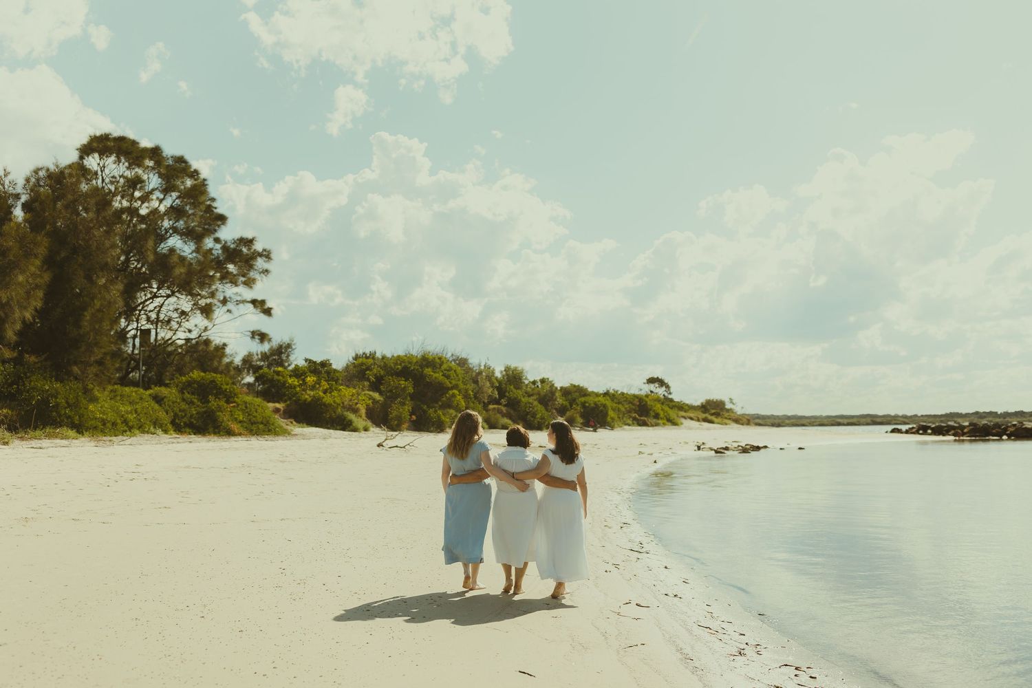 People walking along a pristine white sand beach with trees and blue sky in the background.